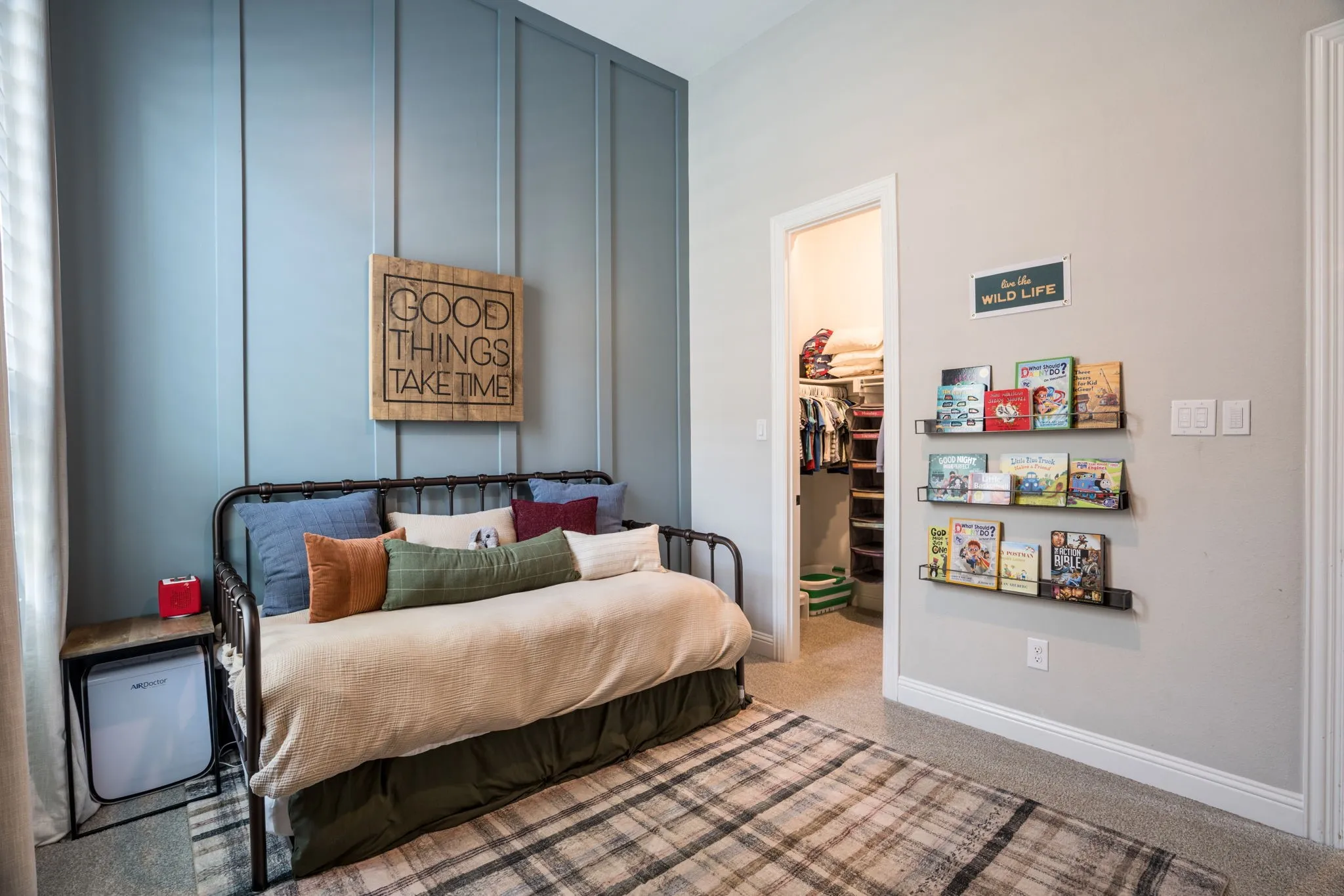 Bedroom featuring a black metal bed frame, plaid area rug, and shiplap accent wall with vertical paneling in soft blue-gray