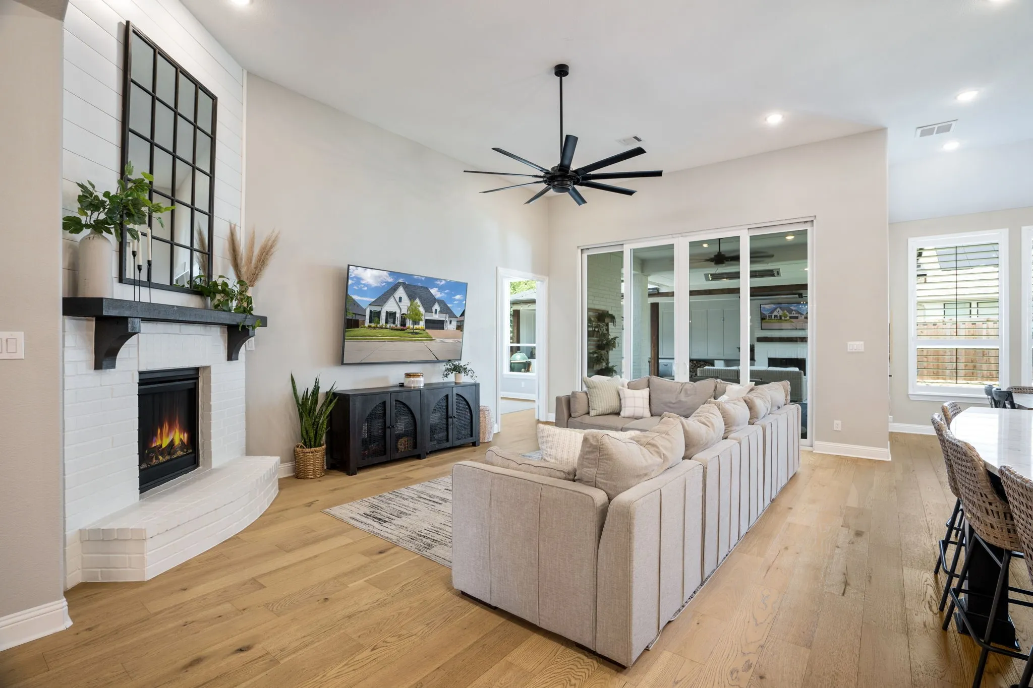 Open-concept living area showcasing hardwood flooring, a gas fireplace with white surround and black metal hearth, built-in media console, and a contemporary ceiling fan