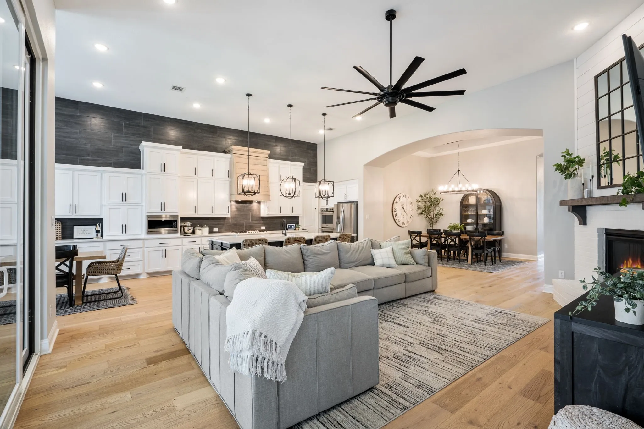 Open-concept living space featuring a gray upholstered sectional sofa, light wood-finish flooring, and a large area rug anchoring the seating arrangement