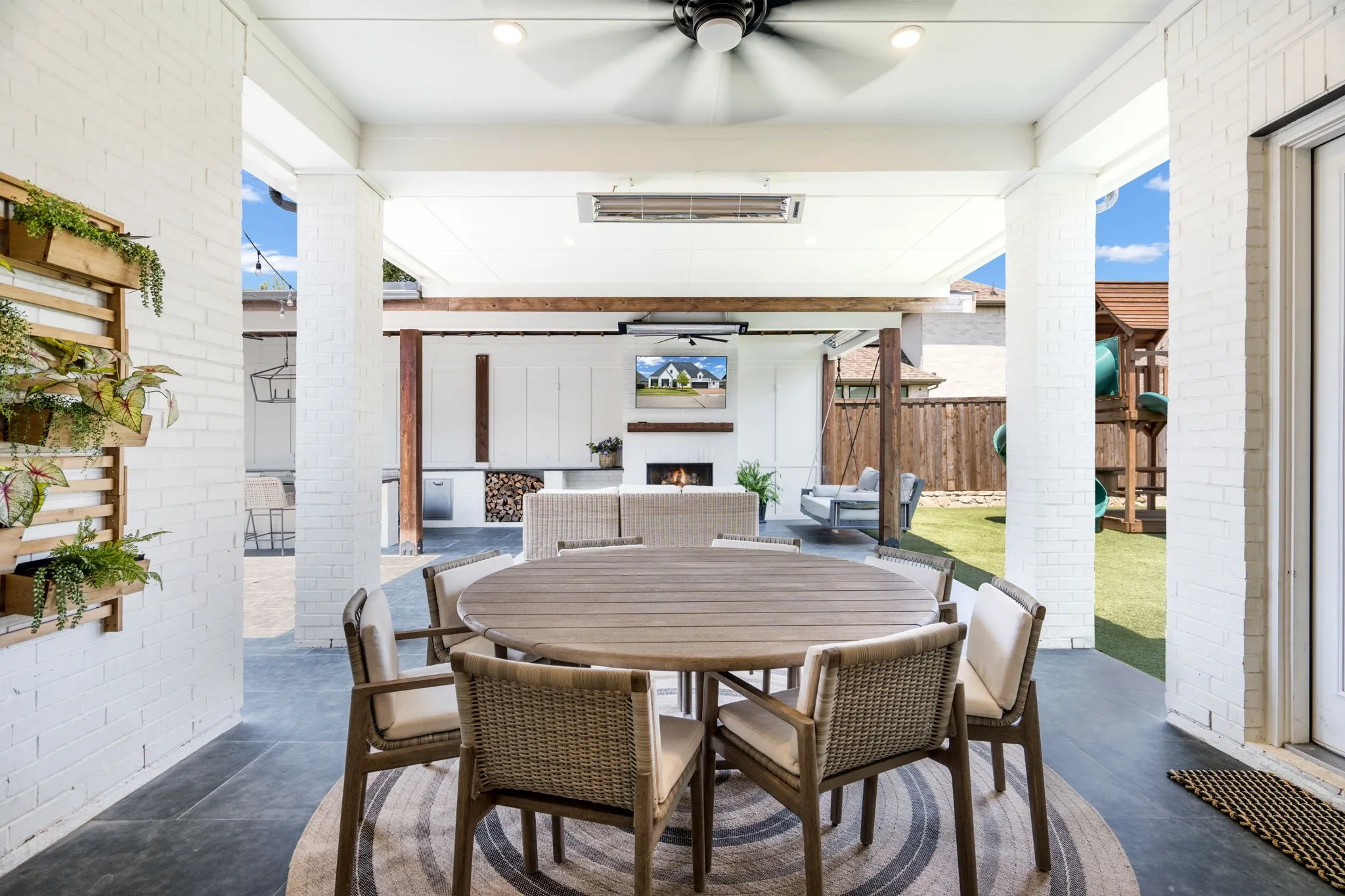 Covered outdoor living space featuring a round wood-finish dining table with seating for four, ceiling fan, and recessed lighting