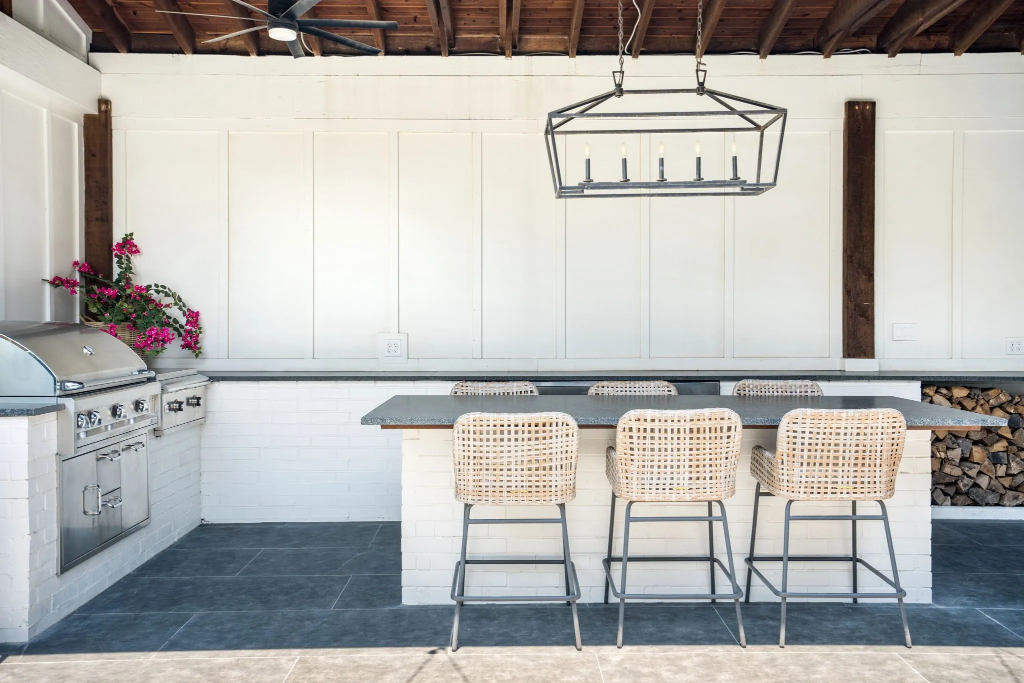 Covered outdoor living area featuring a stone tile floor, built-in fireplace with a wood mantel, and integrated Grill and island