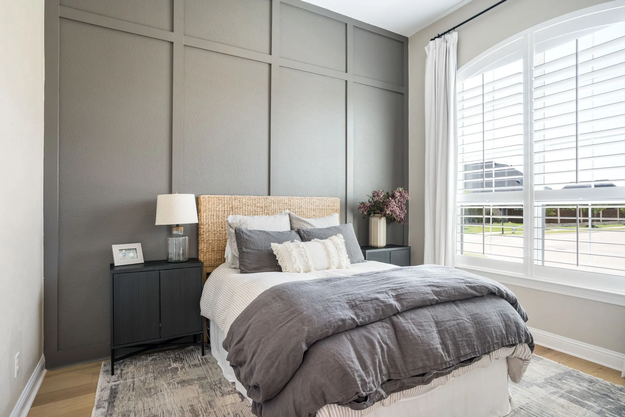 Bedroom featuring a paneled accent wall, arched window with plantation shutters, wood-finish flooring, and a built-in wall sconce