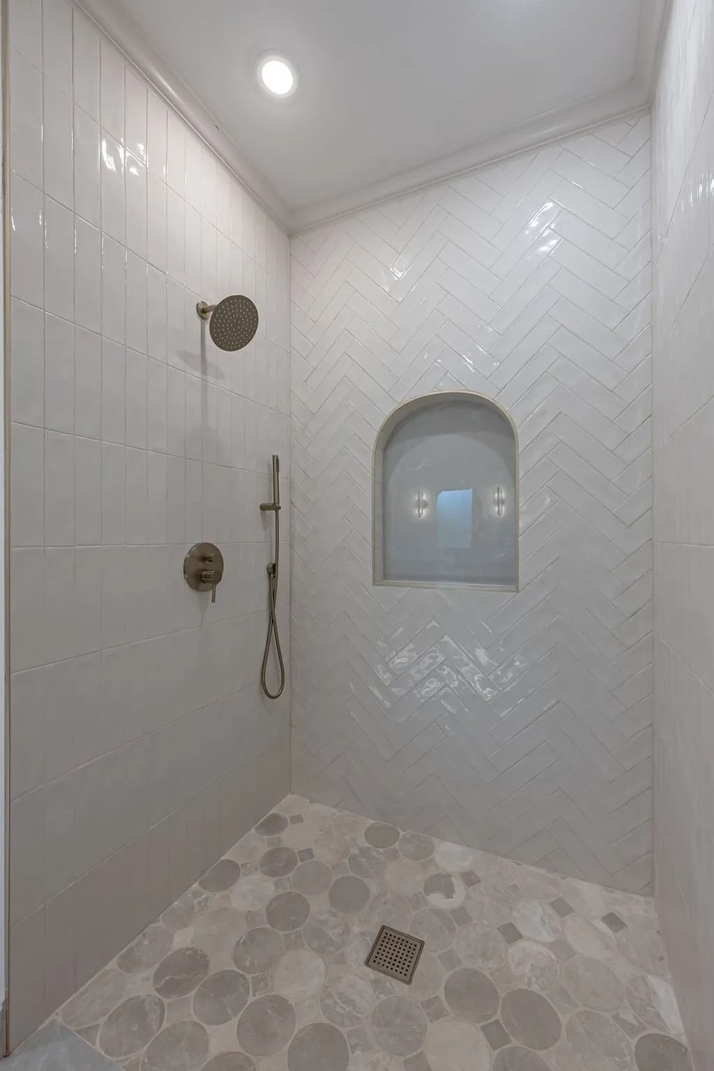 Tiled shower with a rainfall showerhead, handheld spray, and an arched niche