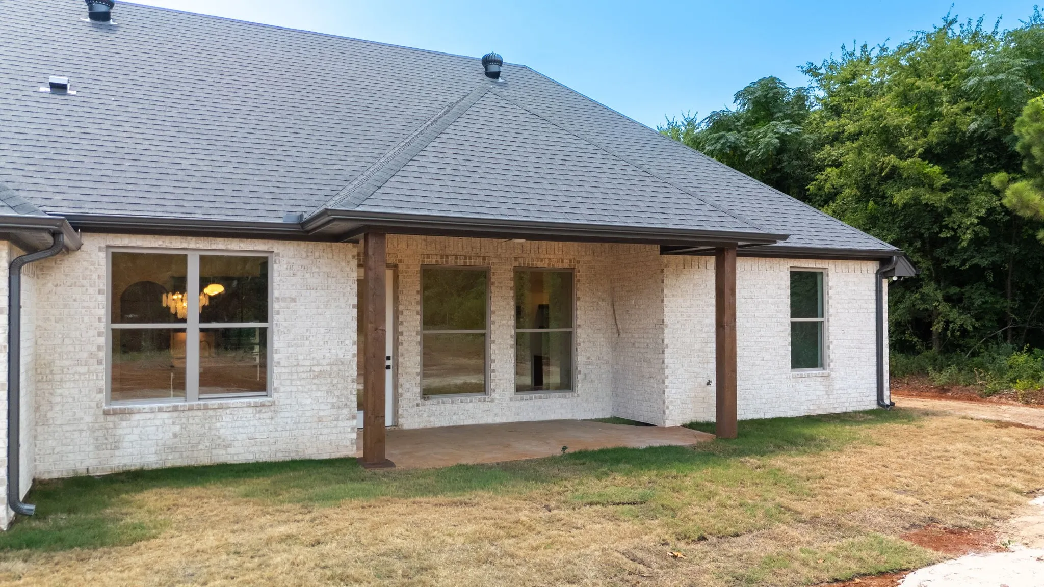 Rear exterior featuring a covered concrete patio supported by wood-finish pillars, white brick façade, and a dark shingle roof