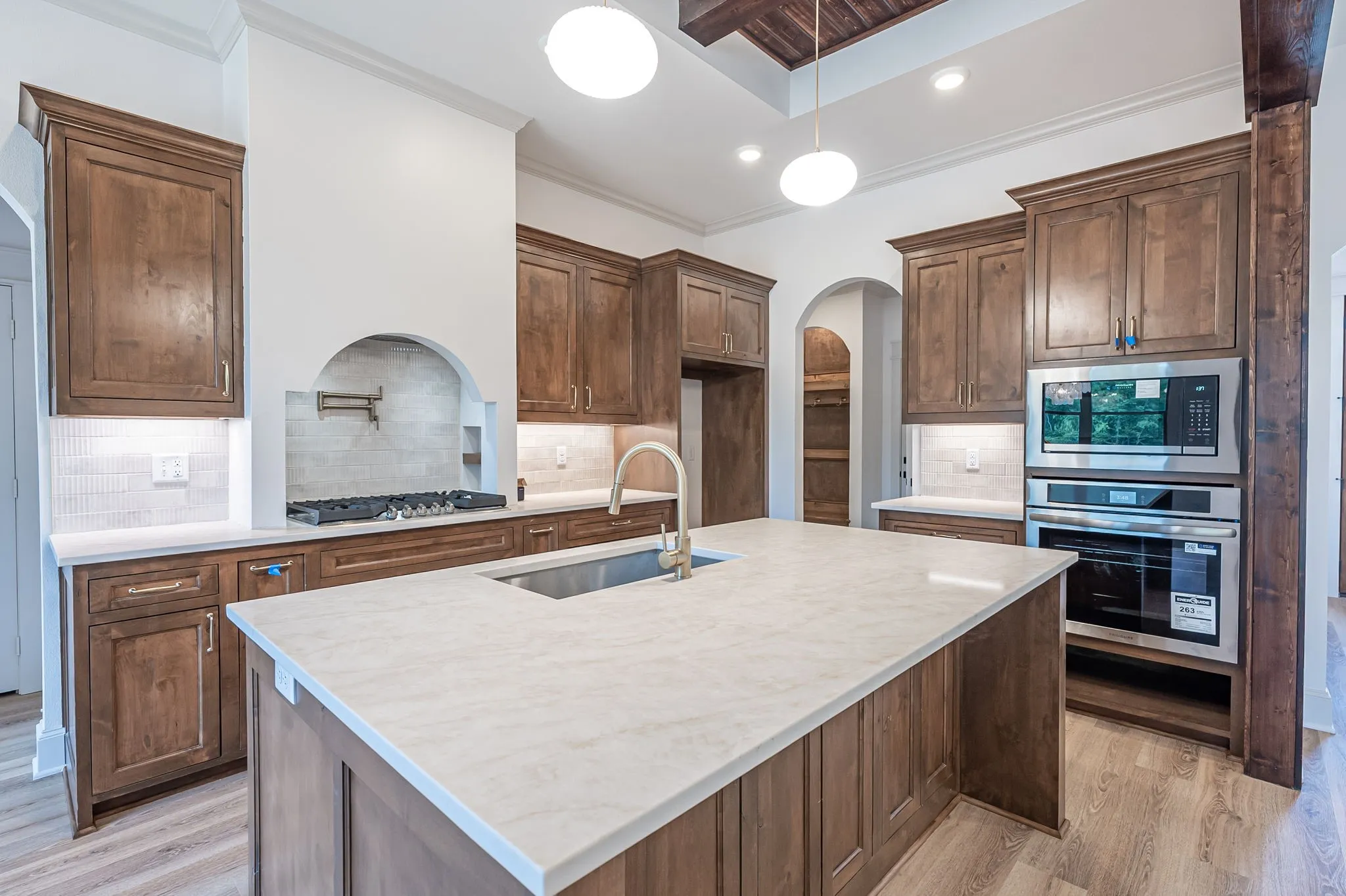 Expansive kitchen island with a light-toned countertop, wood-finish cabinetry, stainless steel appliances, and a gas range