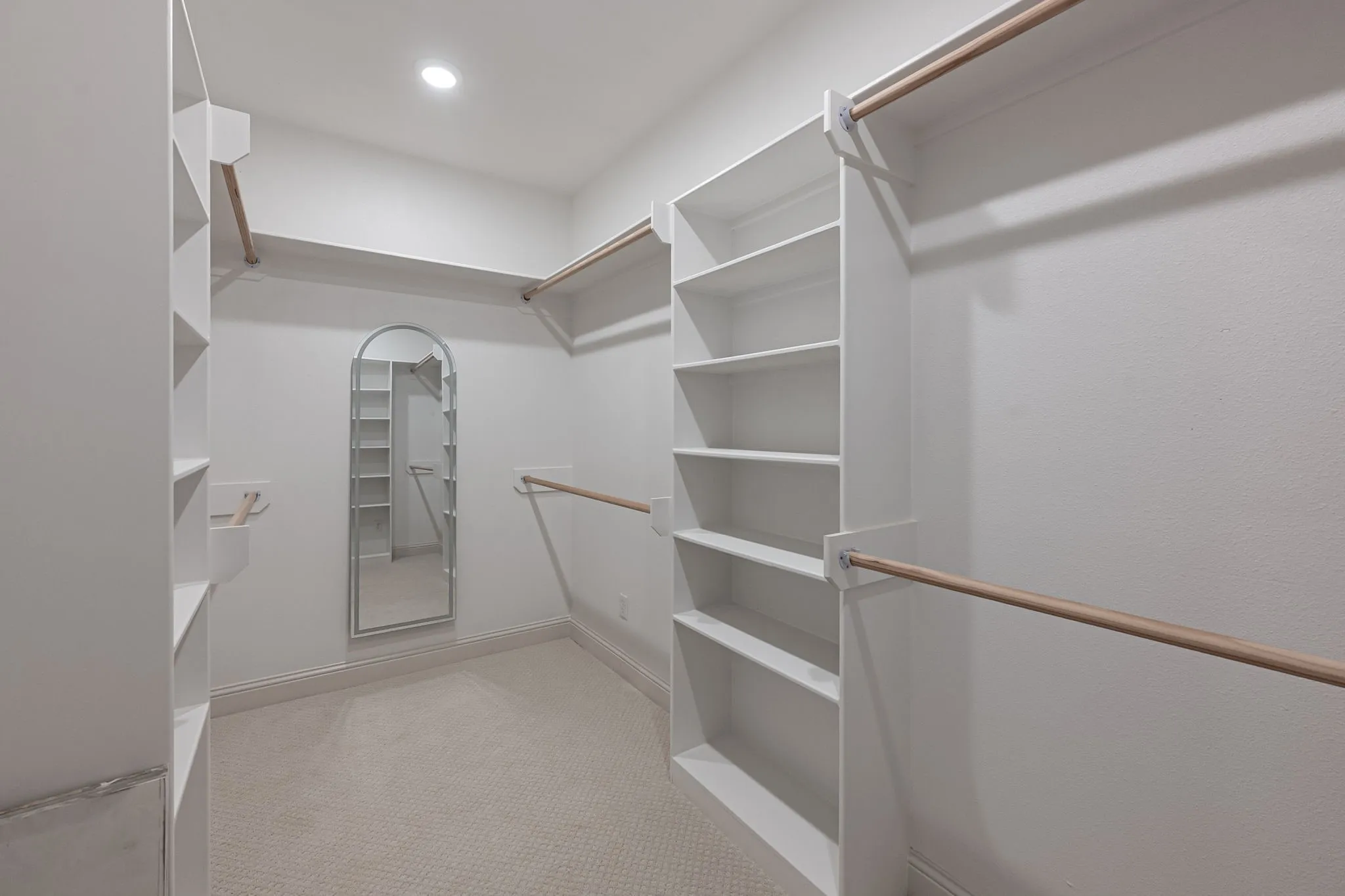 Recessed lighting, wall-mounted mirror, built-in shelving, wood-finish closet rods, and carpet flooring