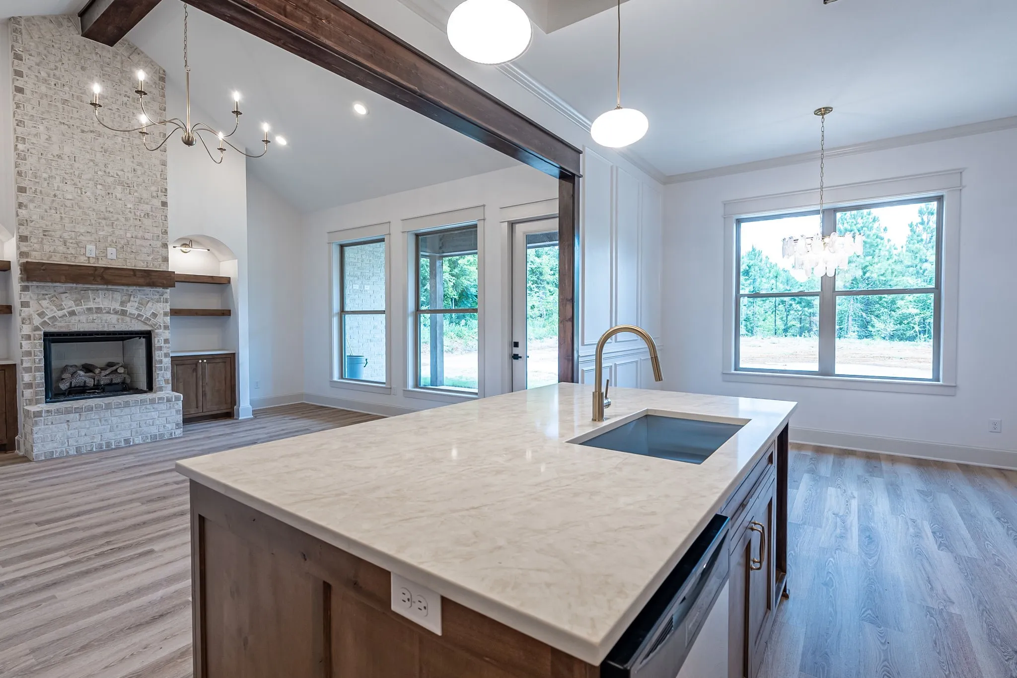 Vaulted ceiling with exposed wood beams, stone fireplace, built-in shelving, wood-finish flooring, and a kitchen island with integrated sink