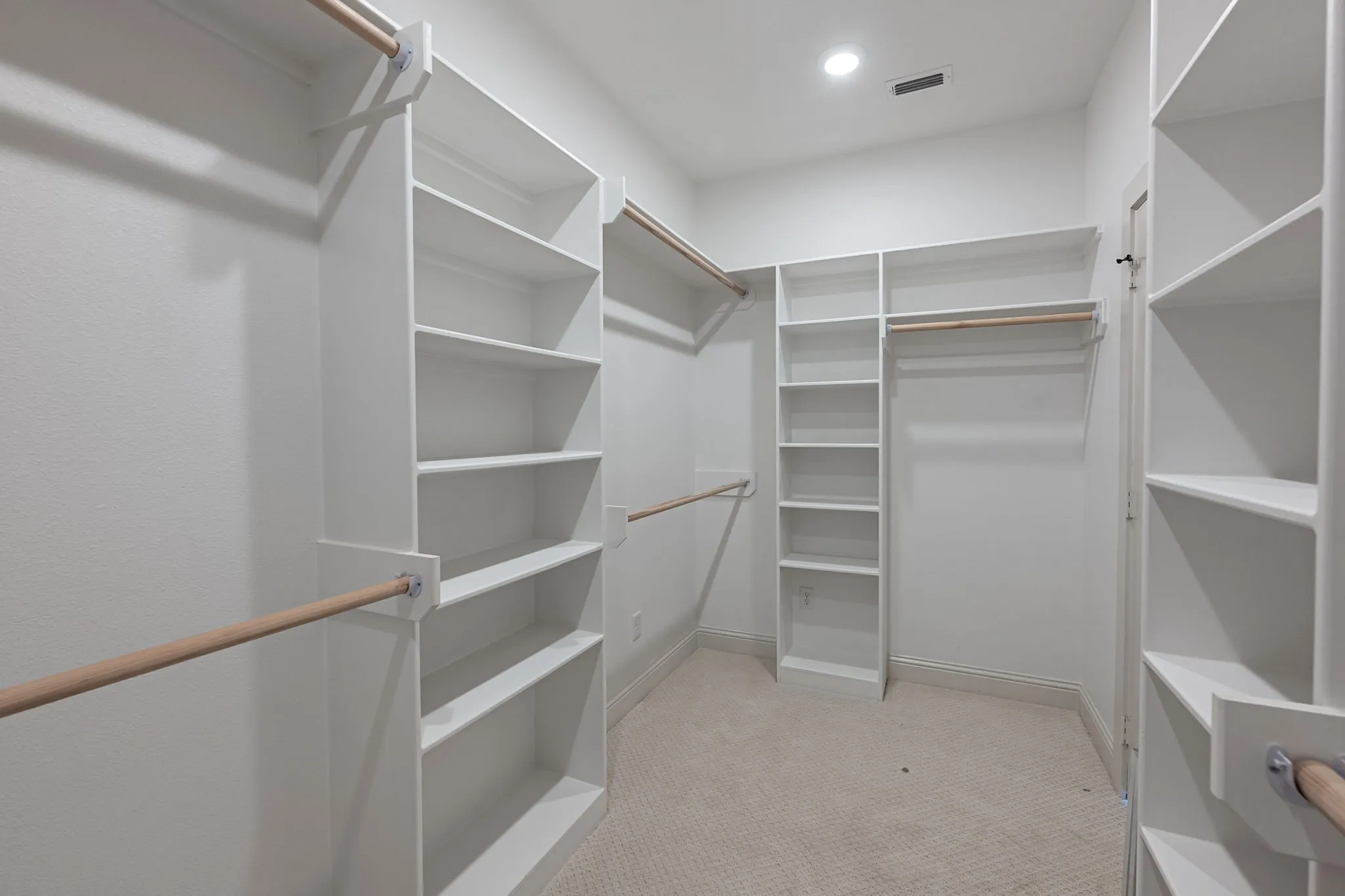 Spacious walk-in closet featuring built-in shelving, multiple hanging rods, and recessed lighting