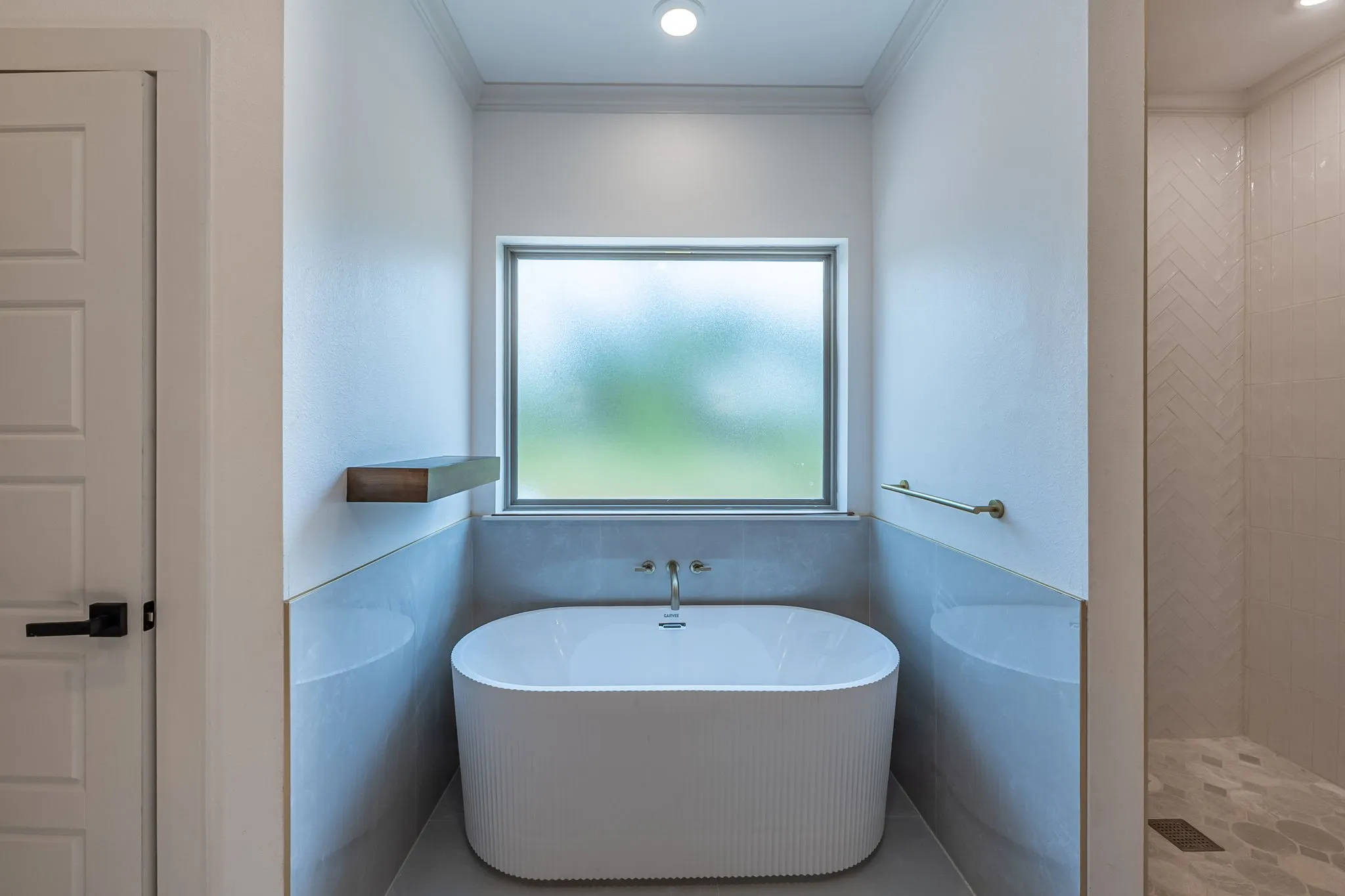 Freestanding soaking tub with a wall-mounted faucet, complemented by a wood-finish floating shelf