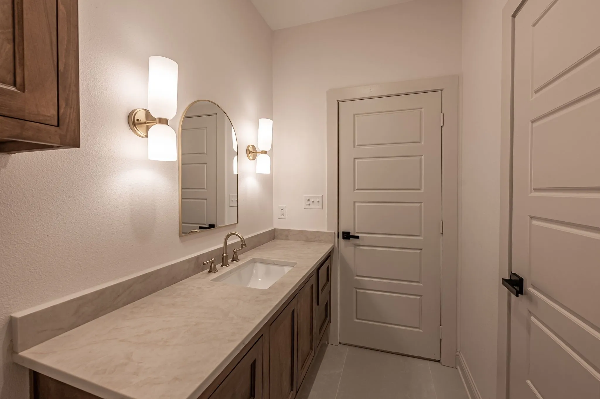 Long single vanity with an integrated sink, brushed gold faucet, and a large arched mirror