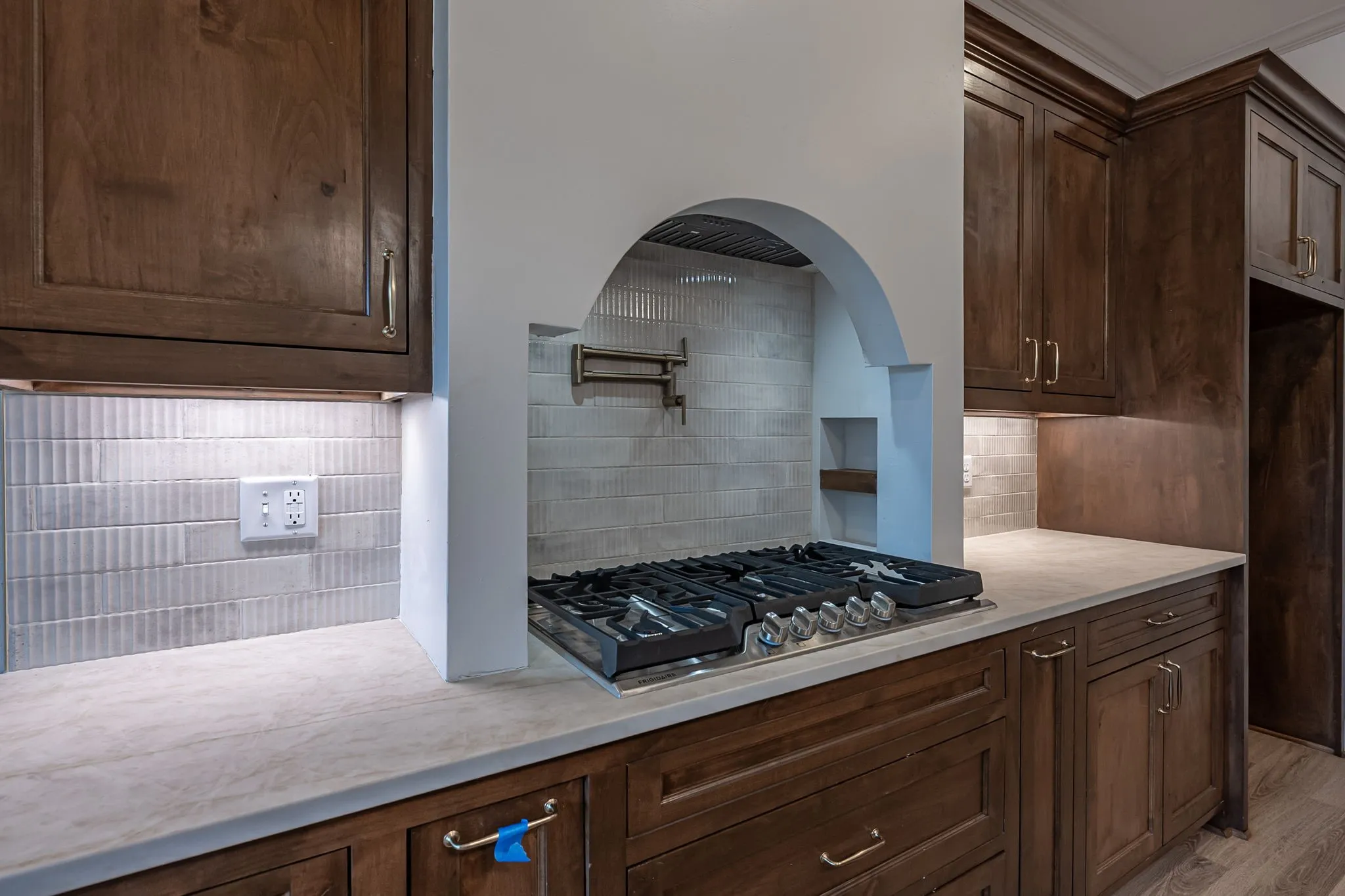 Built-in gas range, arched range hood, wood cabinetry, light-toned countertops, and mosaic tile backsplash