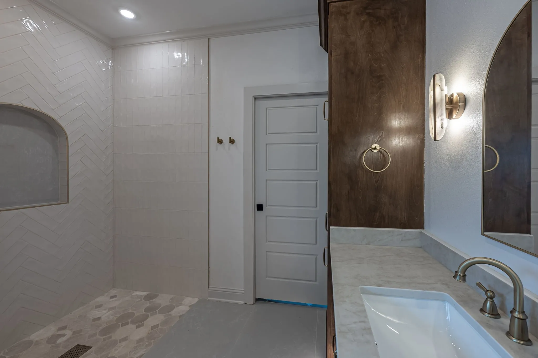 Herringbone-patterned shower wall tile with integrated niche, hexagonal shower floor tile, vanity with integrated sink, brushed metal faucet, and dark wood-finish cabinetry