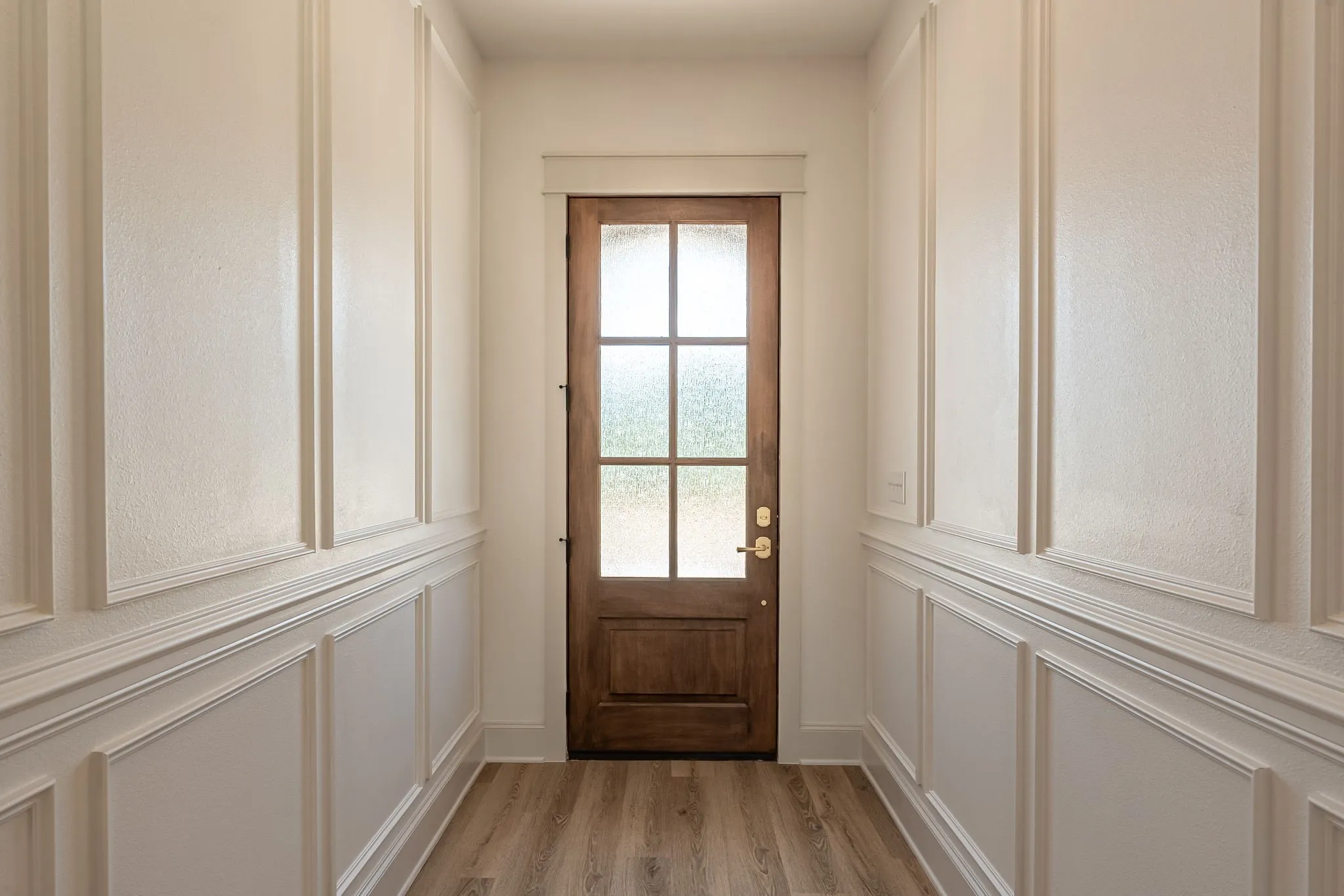 Wood-finish flooring leading to a paneled wood entry door with frosted glass inserts