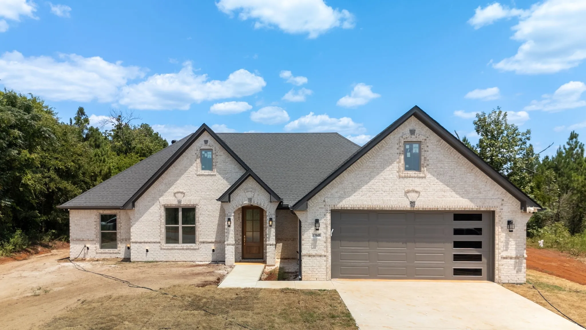 White brick exterior with dark shingle roofing, prominent gables, an arched wood entry door, and a two-car garage with frosted glass inserts