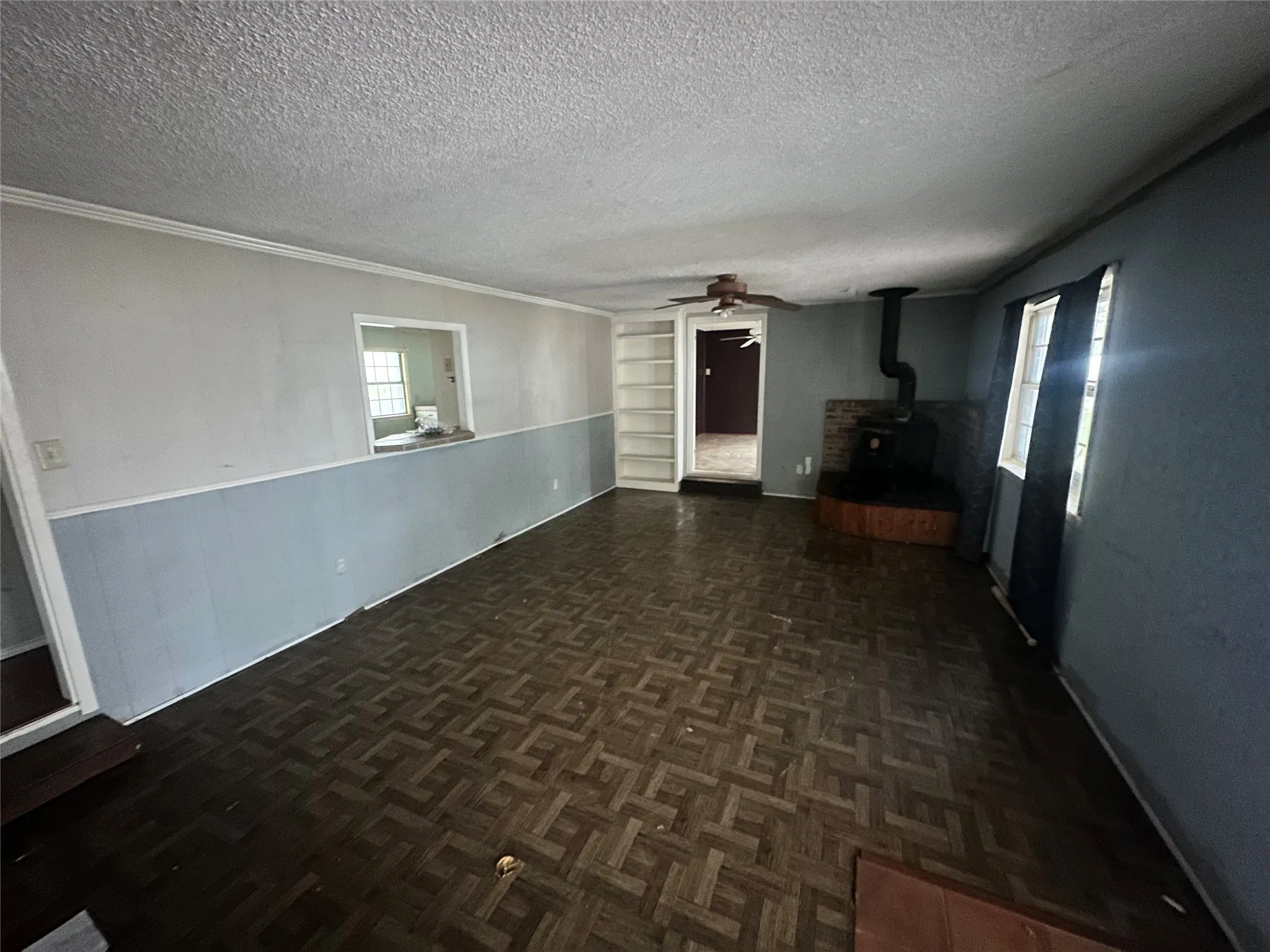 Unfurnished living room featuring built in features, a wood stove, a textured ceiling, and ornamental molding