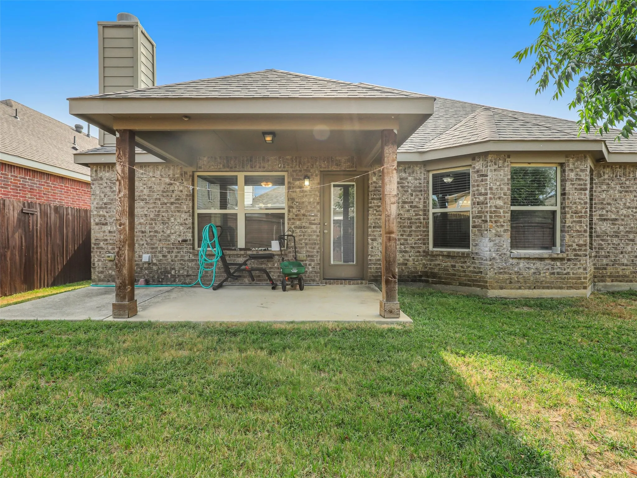 Brick exterior featuring a covered patio with exposed wood posts, a concrete slab, and a fenced perimeter