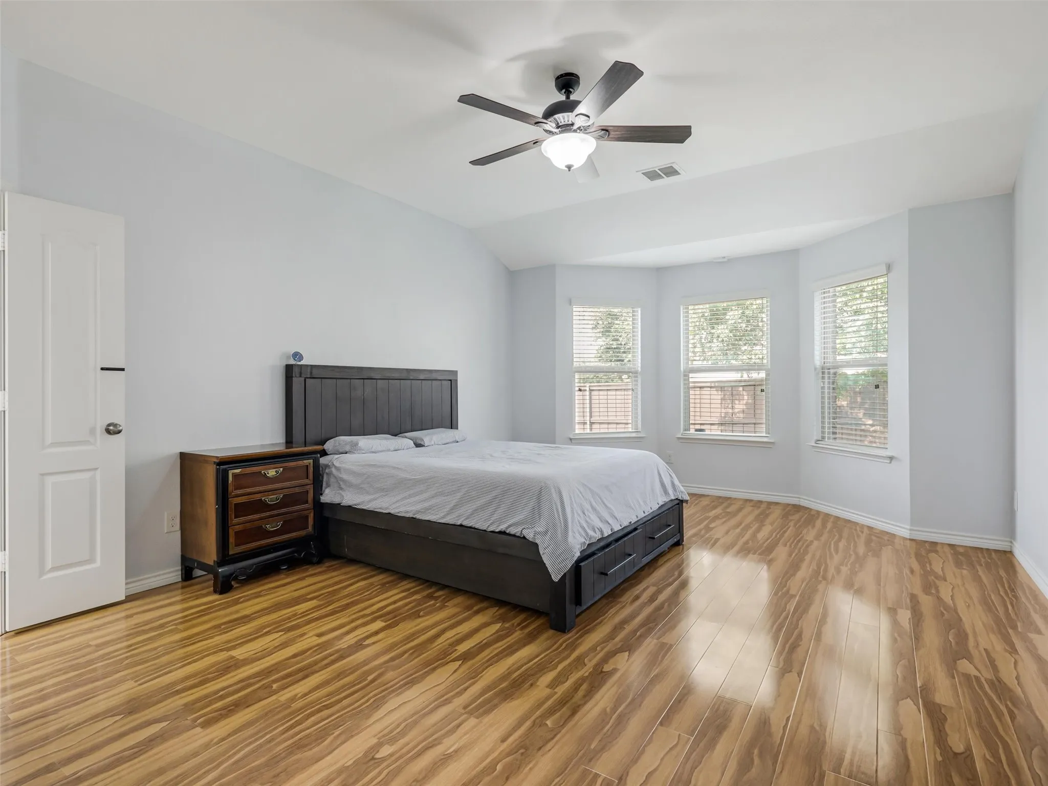 Spacious bedroom featuring wood-finish flooring, a ceiling fan with integrated lighting, and a bay window configuration with three individual windows