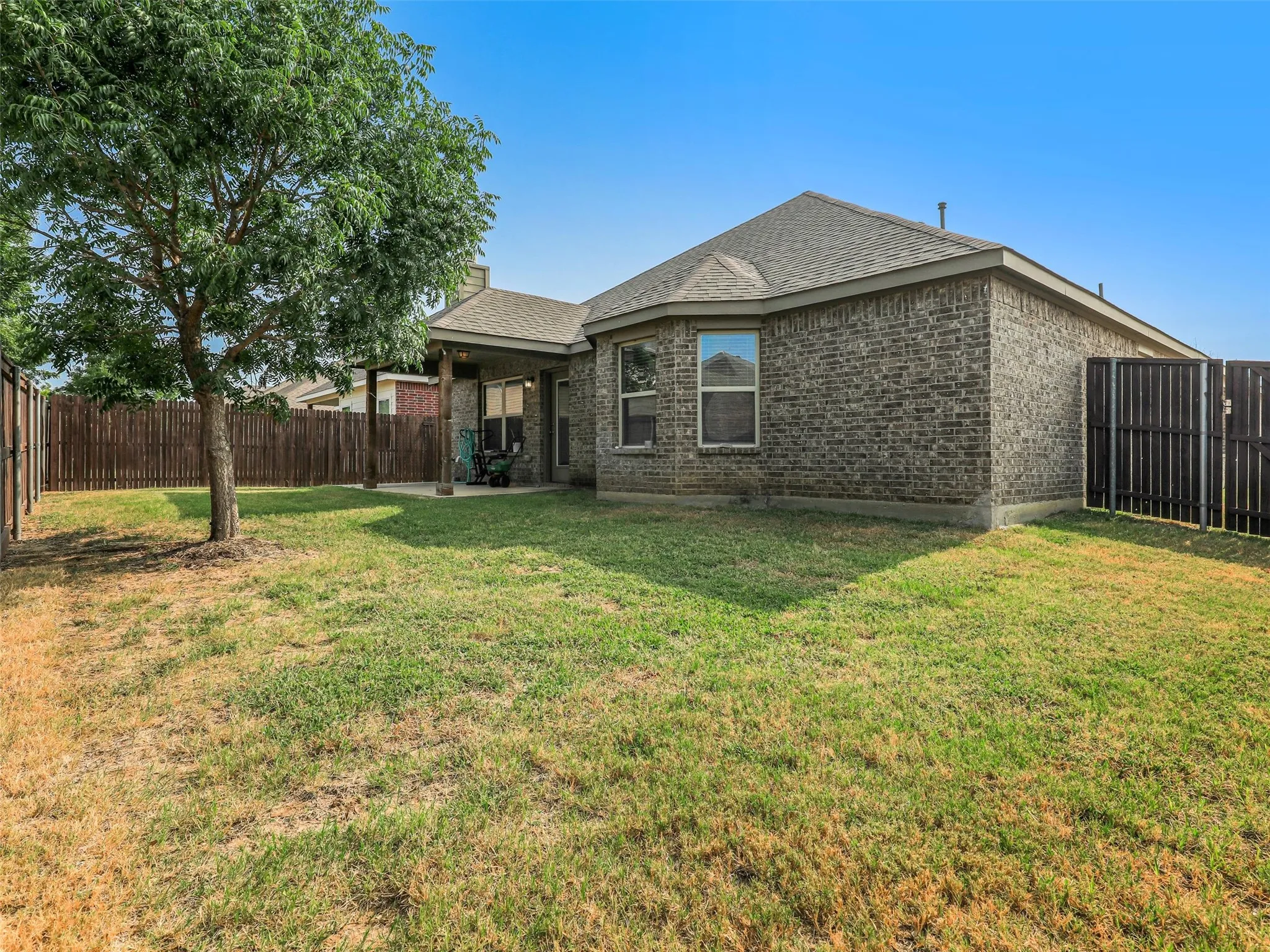 Expansive rear yard featuring a covered patio, full brick exterior, fenced perimeter, and a mature shade tree