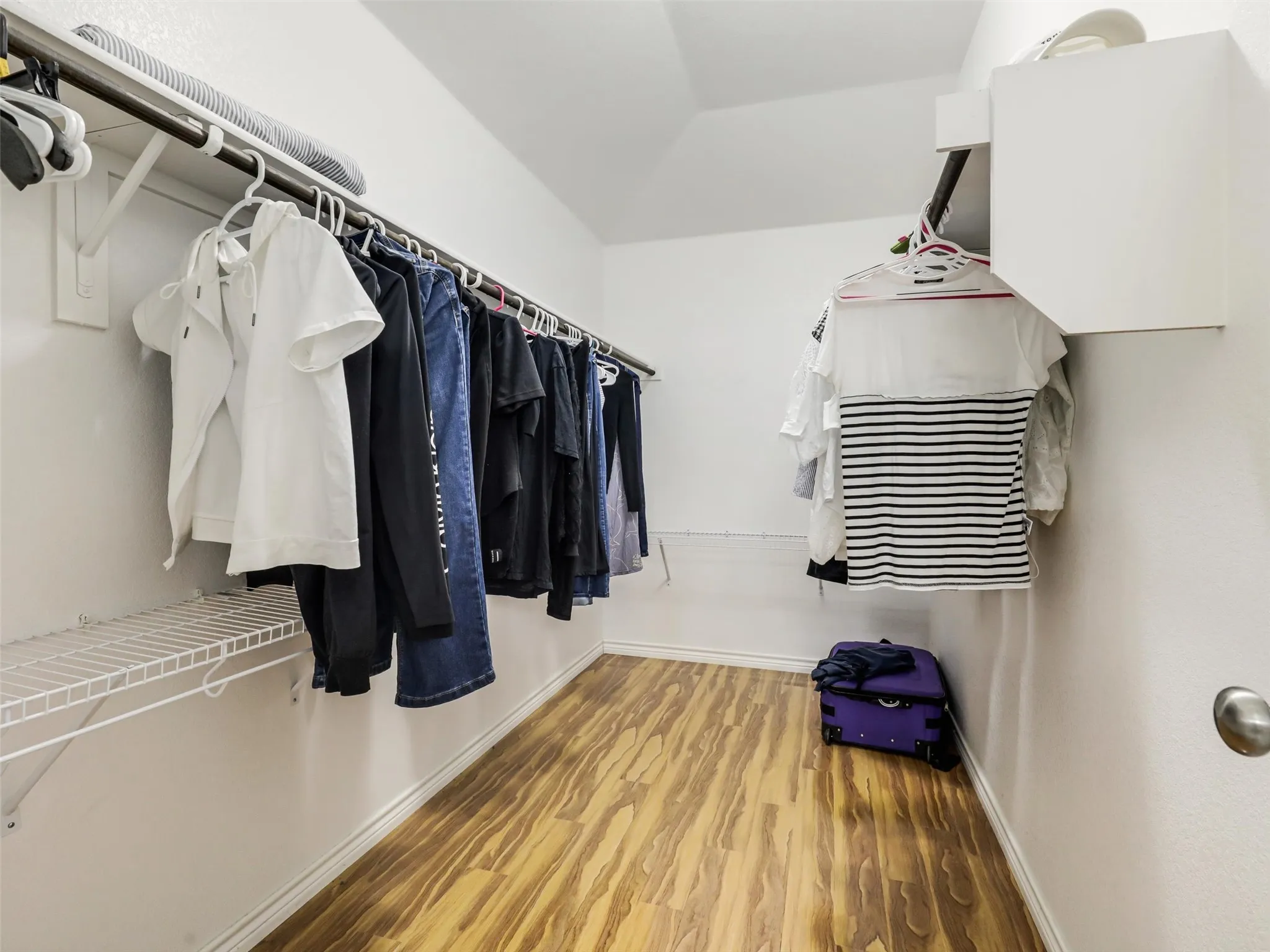 Walk-in closet featuring wood-finish flooring, white walls, multiple hanging rods, wire shelving, and built-in white cabinetry