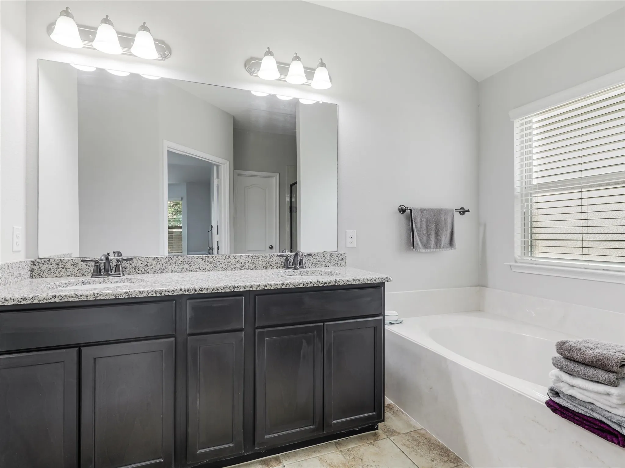 Bathroom featuring a dual vanity with granite countertops, dark wood cabinetry, and an undermount soaking tub