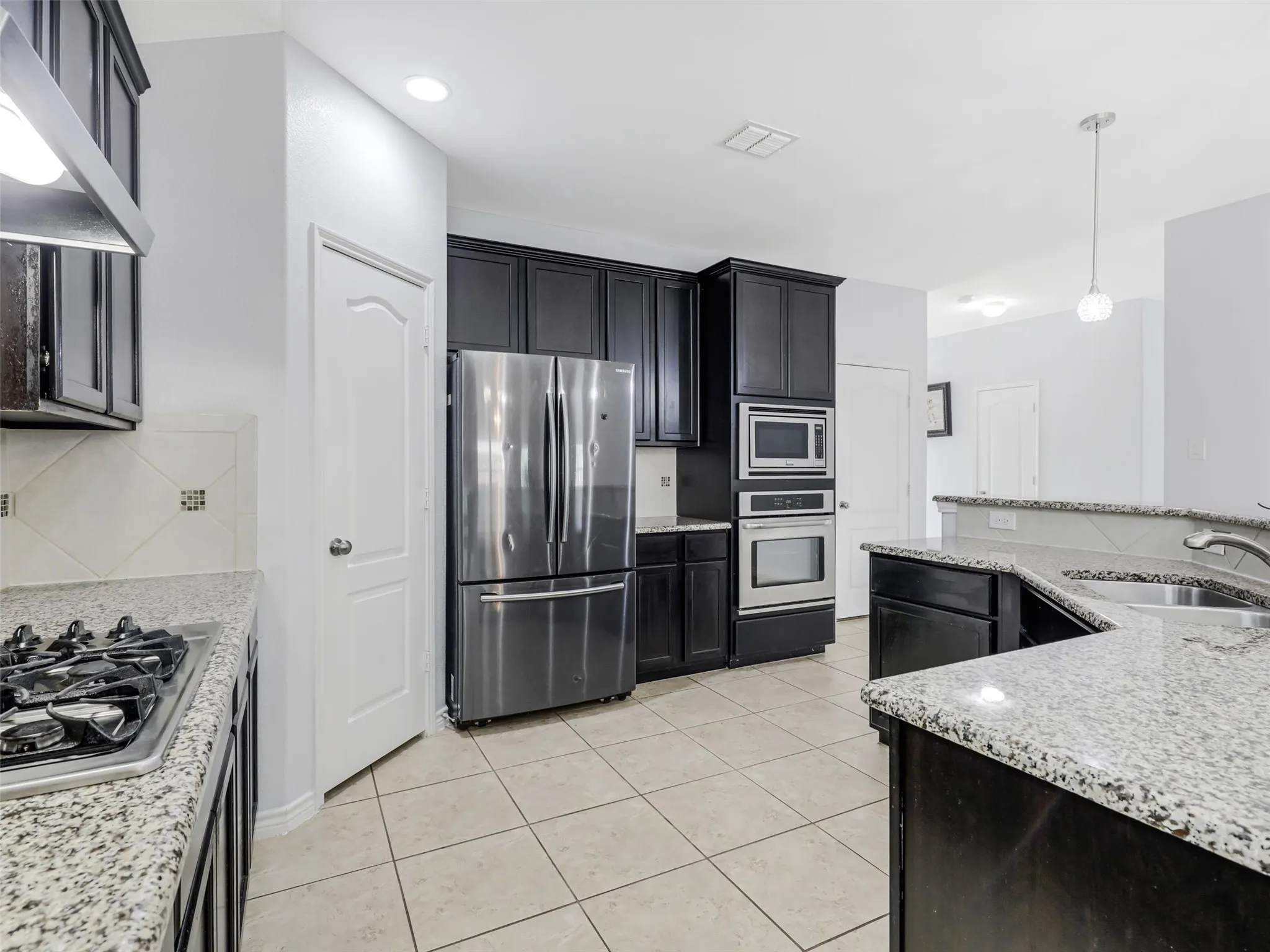 Kitchen featuring dark cabinetry, speckled countertops, stainless steel appliances, a gas cooktop, and tile flooring