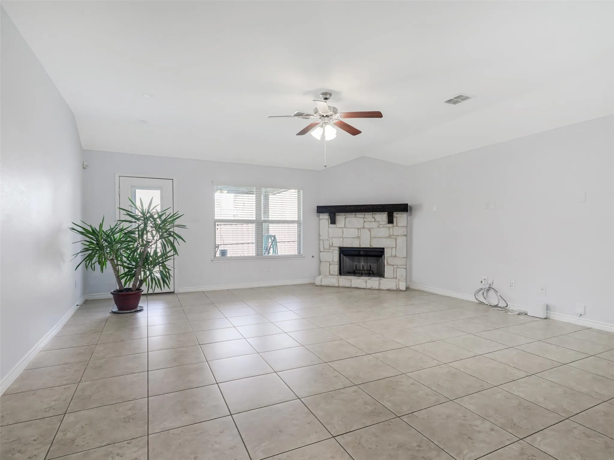 Spacious living area featuring neutral tile flooring, a stone-clad fireplace with a dark wood mantel, and a ceiling fan