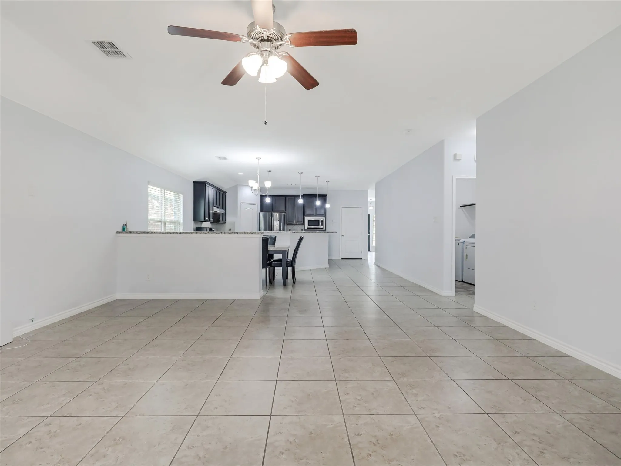 Open-concept living area featuring light-toned tile flooring, a ceiling fan with integrated lighting, and a half-wall partition