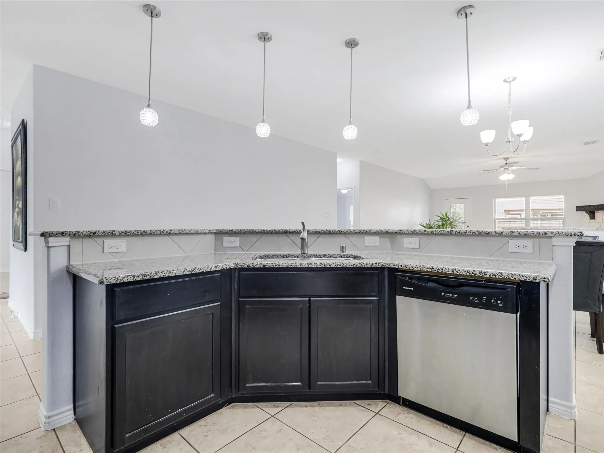 Kitchen peninsula featuring dark cabinetry, granite-finish countertops, a stainless steel dishwasher, and a tile backsplash