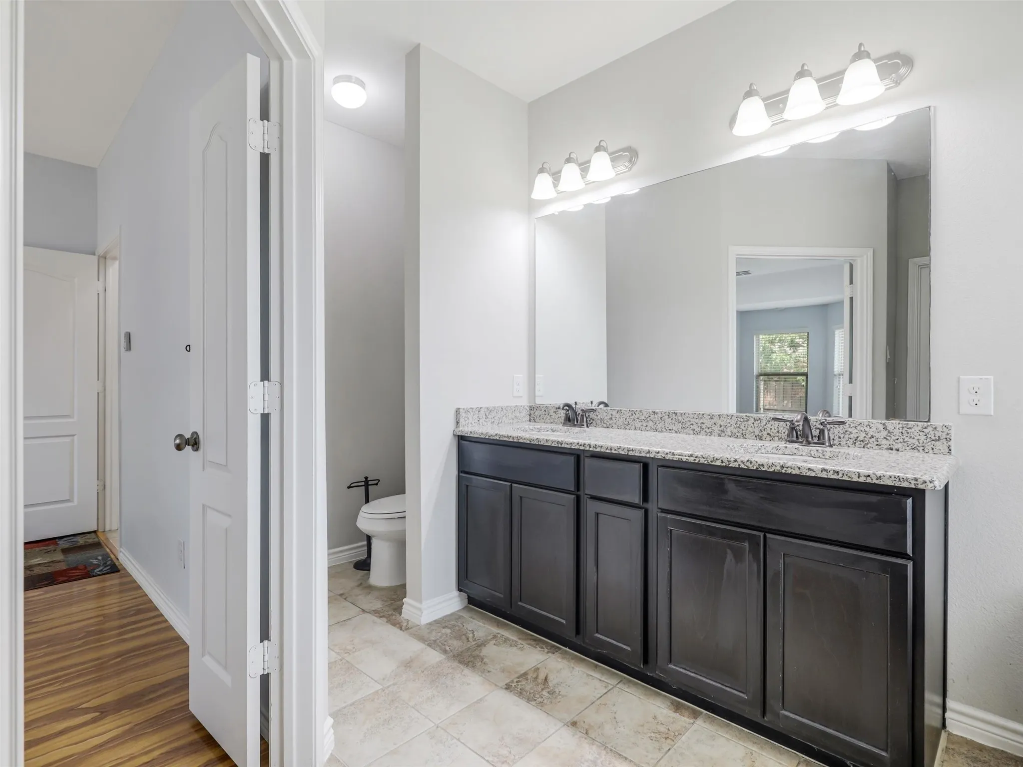 Spacious bathroom featuring a dual vanity with a light-colored countertop, dark wood-finish cabinetry, a large wall-mounted mirror, and tile flooring
