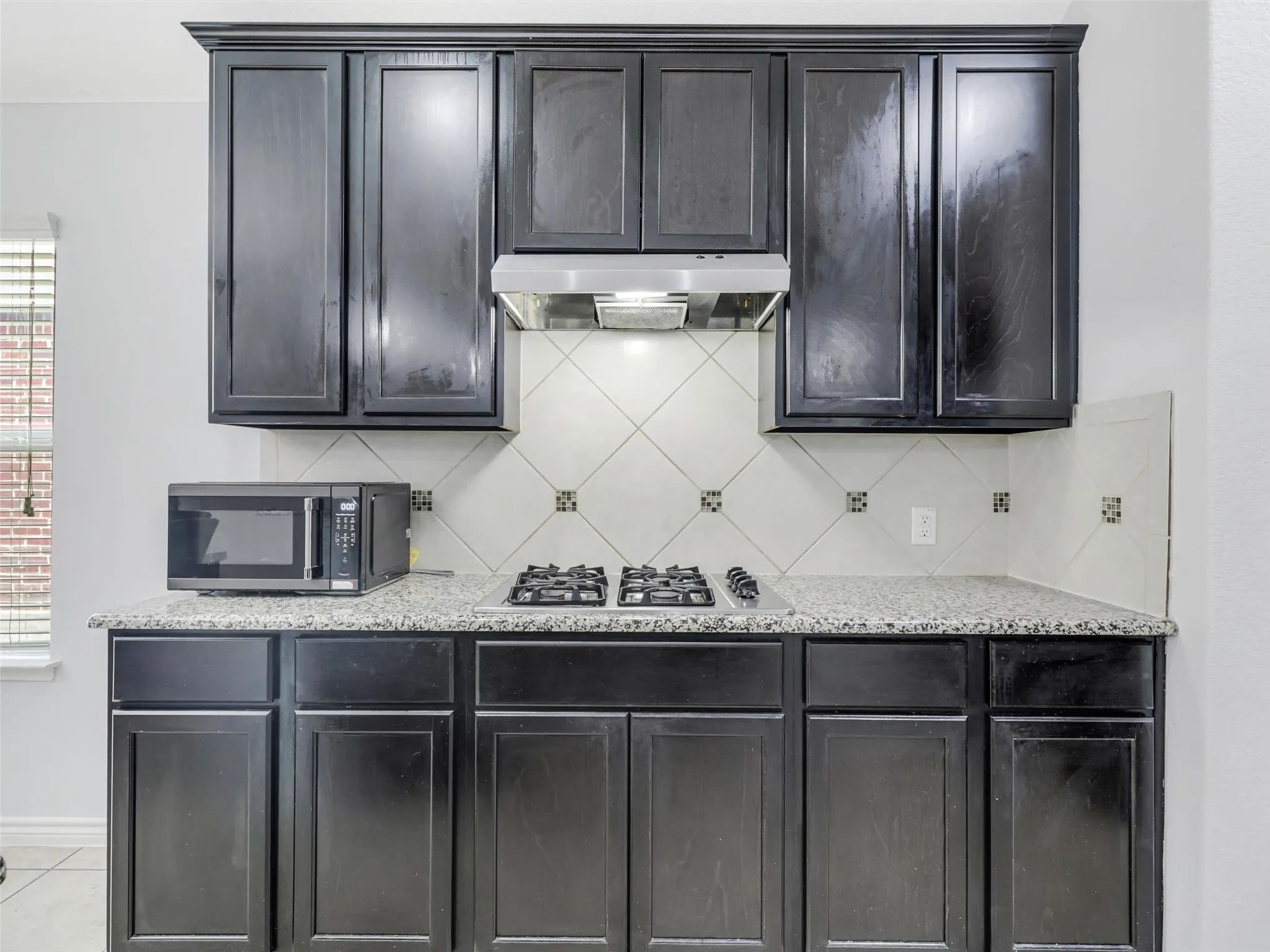 Kitchen featuring dark wood cabinetry, light speckled countertops, a gas cooktop, and a tile backsplash with decorative accents