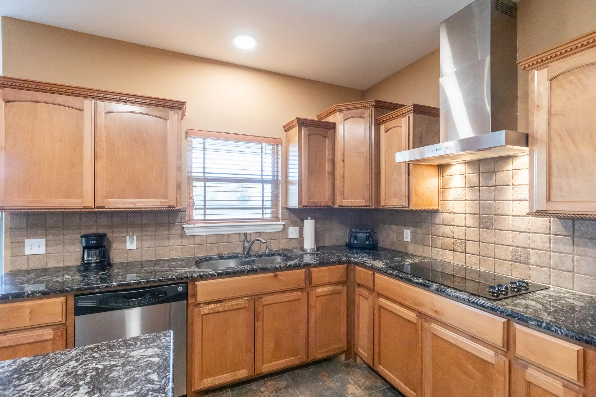 Modern kitchen featuring granite-look countertops, a stainless steel dishwasher, a built-in cooktop, and a stainless steel range hood