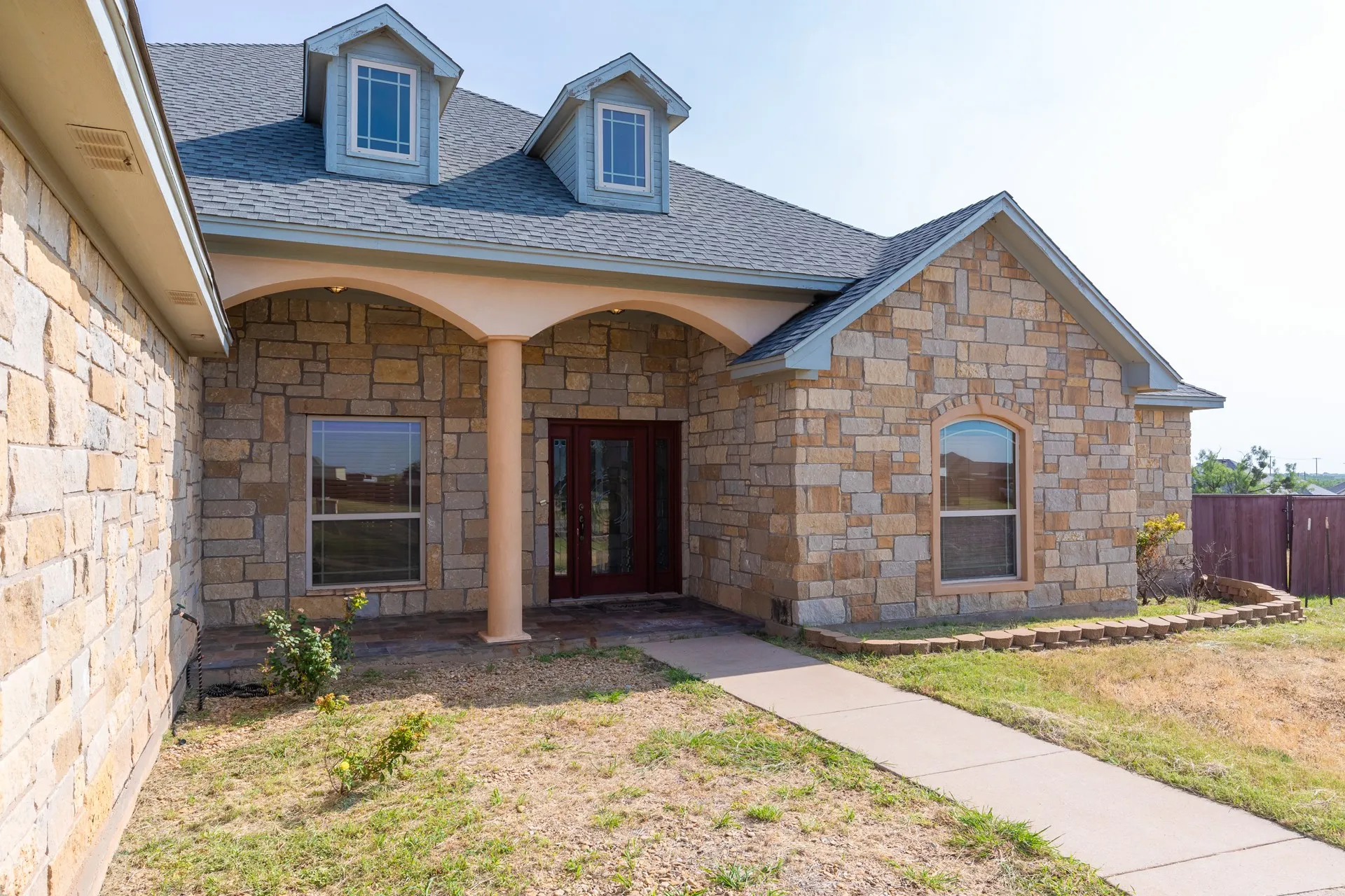 Charming brick residence featuring a welcoming front elevation with arched entryways, dual dormer windows, and a covered entry portico