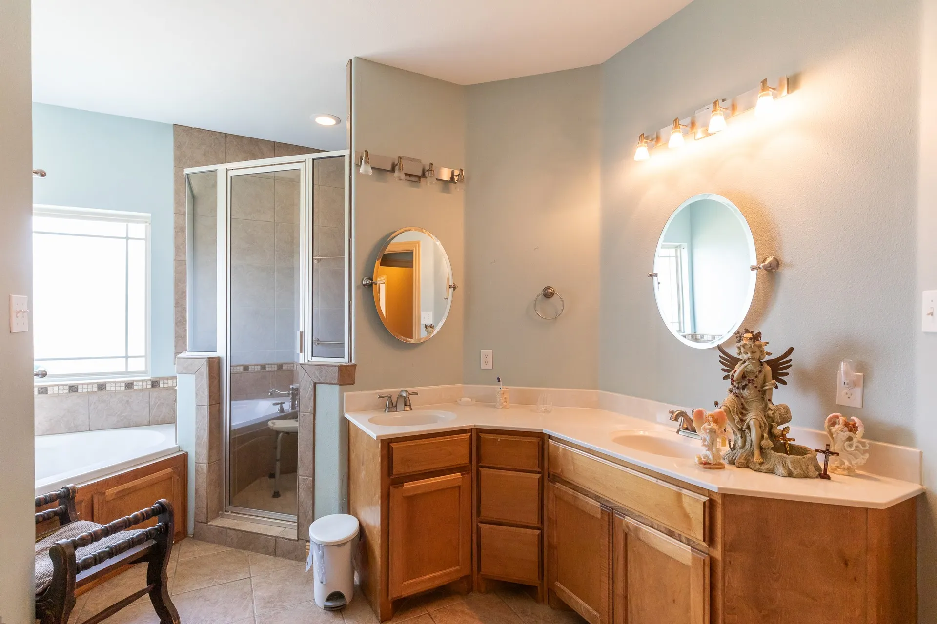 Bathroom featuring a corner soaking tub, a separate glass-enclosed shower, a dual vanity with light-colored countertops, and tile flooring