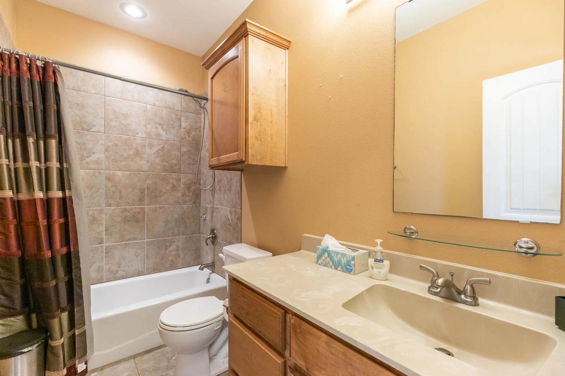 Bathroom featuring a tub and shower combination with tiled surround, a light-toned vanity with an integrated sink, a rectangular mirror, and an overhead lighting fixture