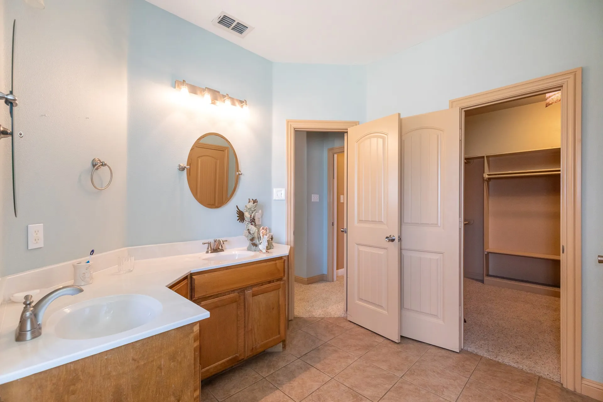 Bathroom featuring a corner vanity with dual sinks, light wood cabinetry, and a white countertop