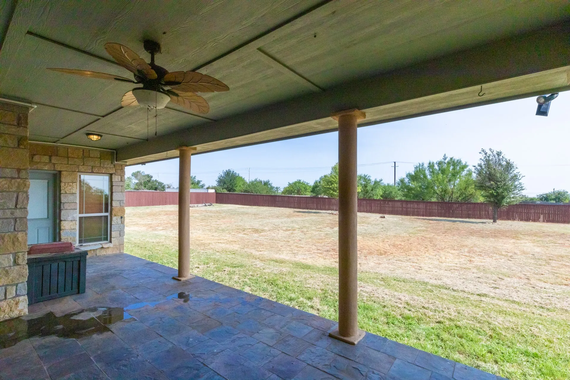 Expansive covered patio featuring stamped concrete flooring, a ceiling fan, and stone pillar supports
