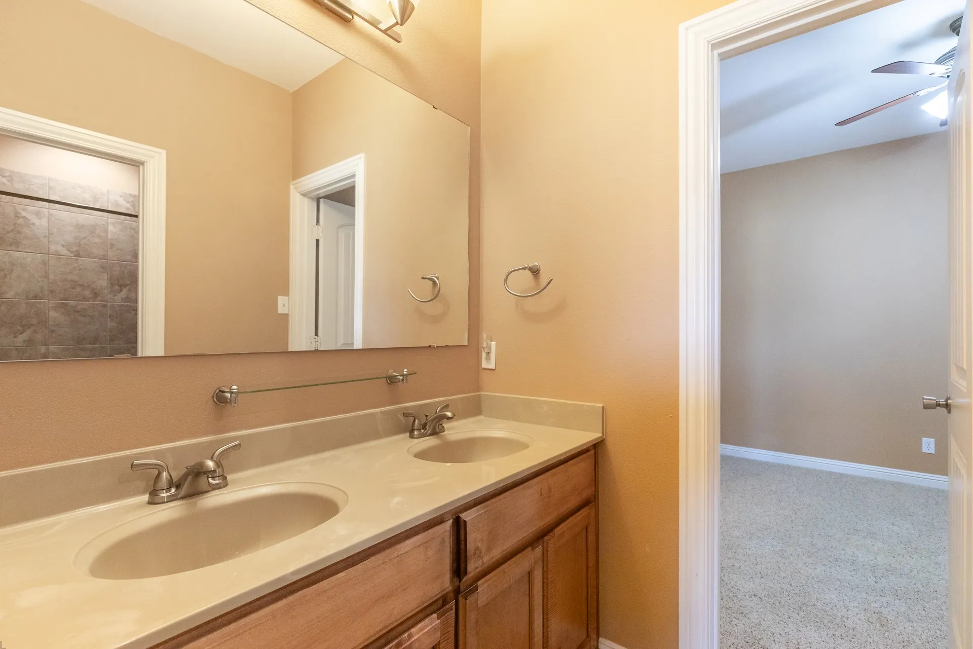 Bathroom featuring a dual vanity with light-toned countertops, wood cabinetry, and brushed nickel fixtures