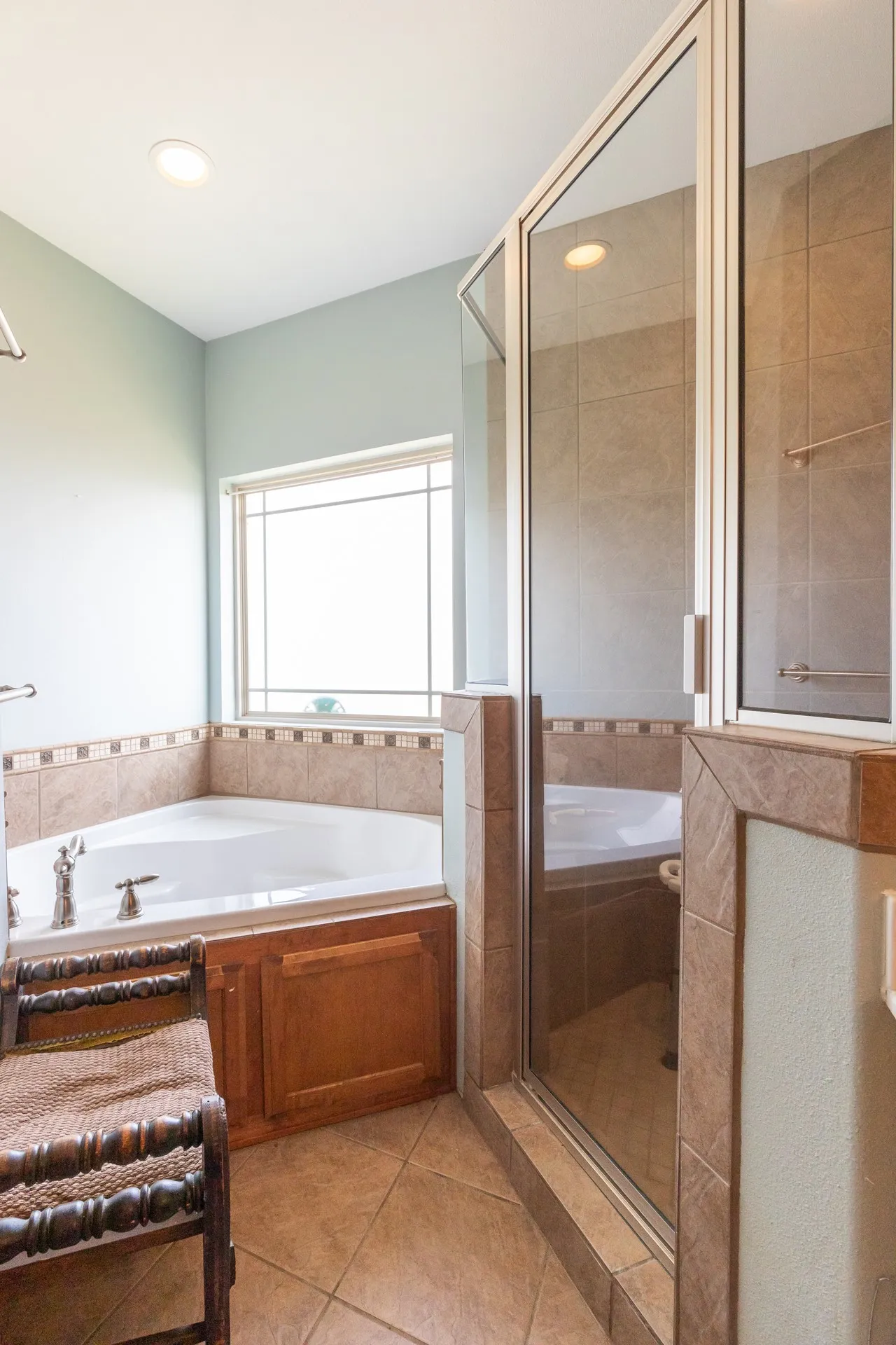 Bathroom featuring a corner soaking tub with tile surround, a separate glass-enclosed shower, and a large window with privacy grid