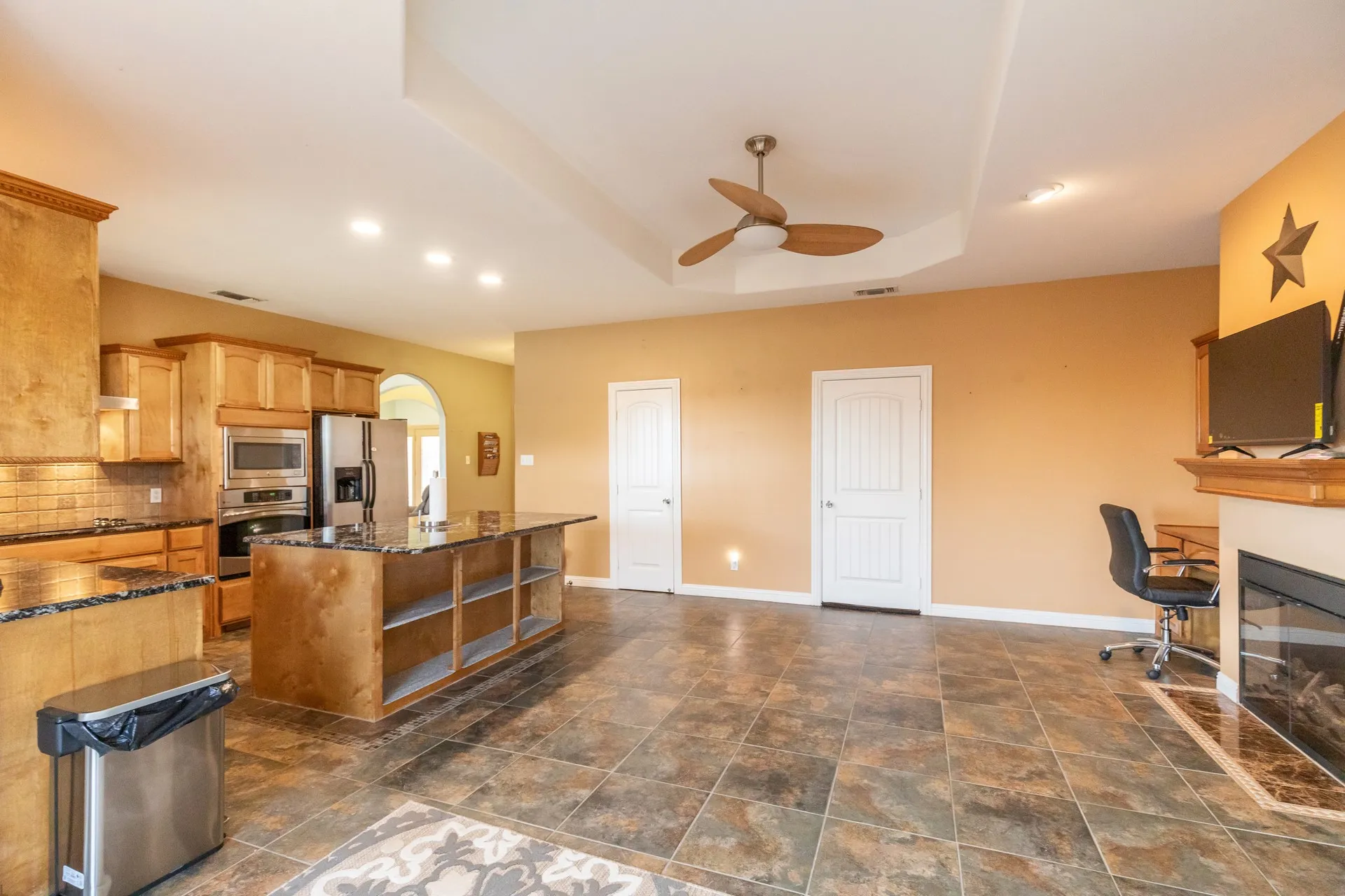 Spacious open-concept area featuring a kitchen with wood cabinetry, dark countertops, and stainless steel appliances