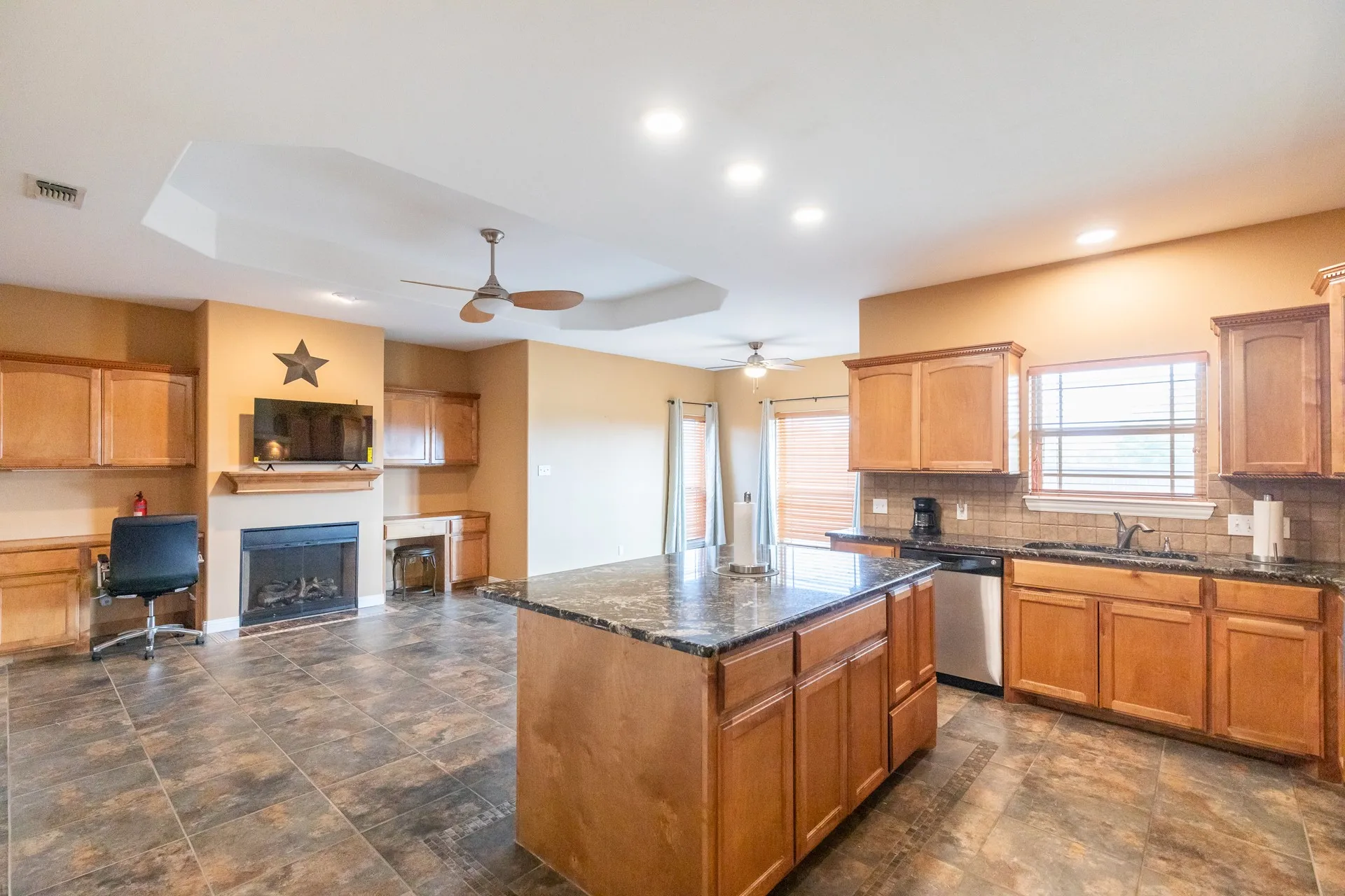 Spacious open-concept kitchen and living area featuring a large center island with a stone-finish countertop, light wood cabinetry, and stainless steel appliances