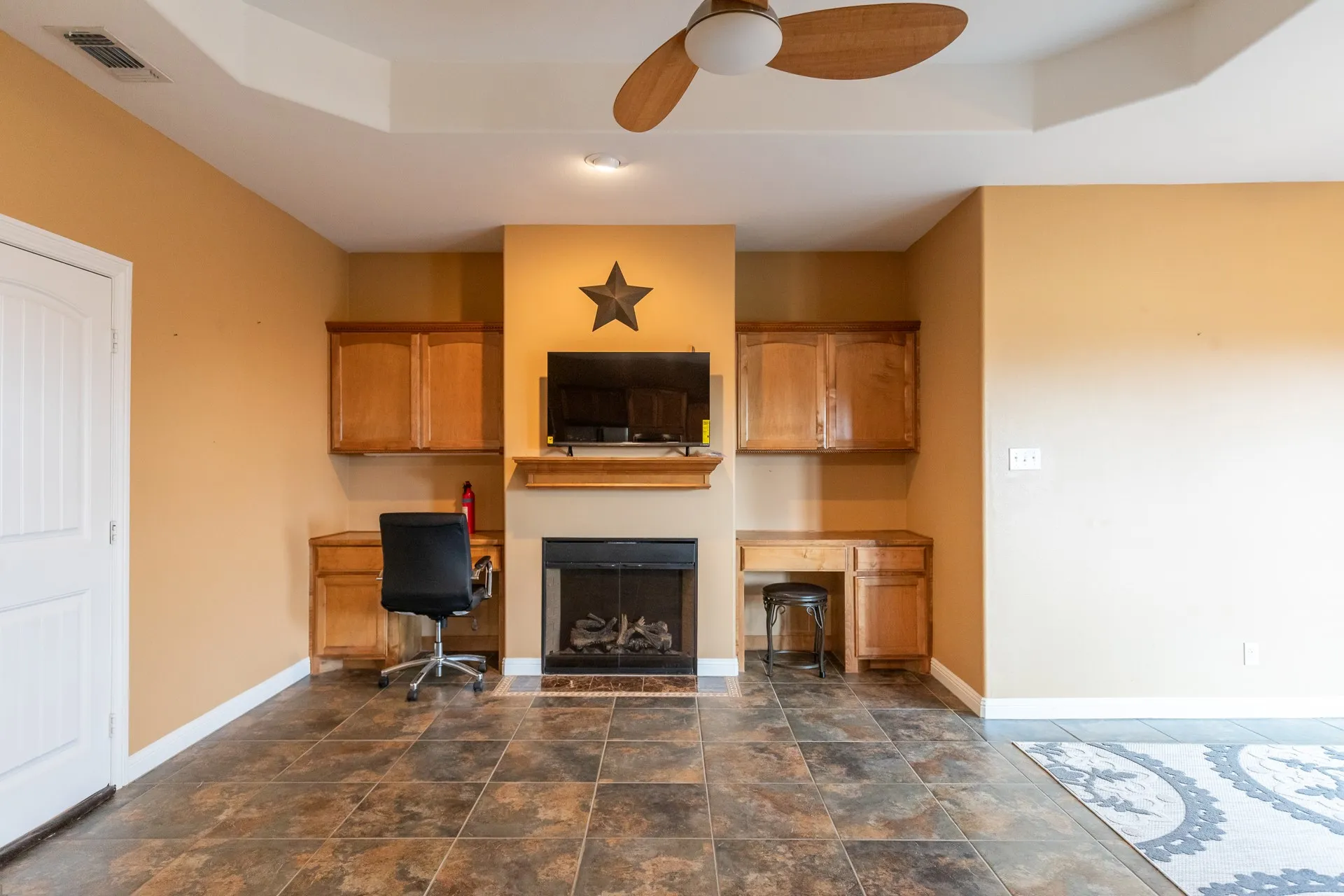 Spacious family room featuring a wood-finish tile floor, ceiling fan with wooden blades, and a striking focal point with a fireplace flanked by built-in cabinetry