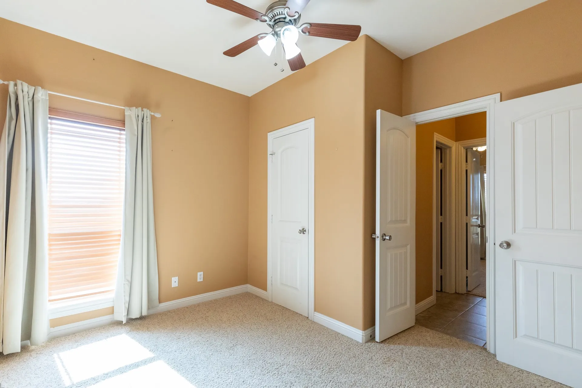 Carpeted room featuring a ceiling fan with light fixture, window with blinds and curtains, and multiple white panel doors