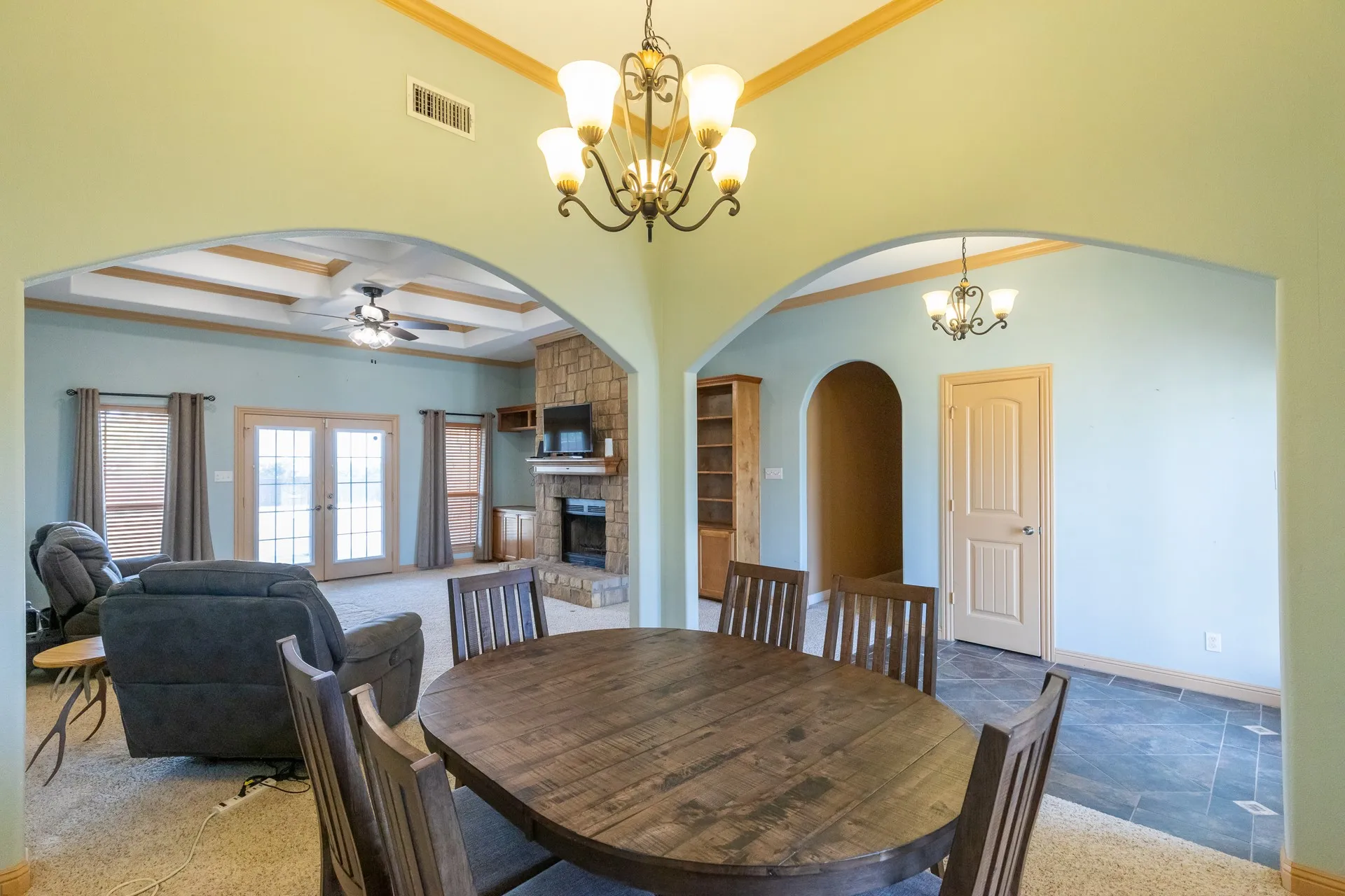 Open-concept interior featuring arched doorways, a stone-clad fireplace, and a tray ceiling with a ceiling fan