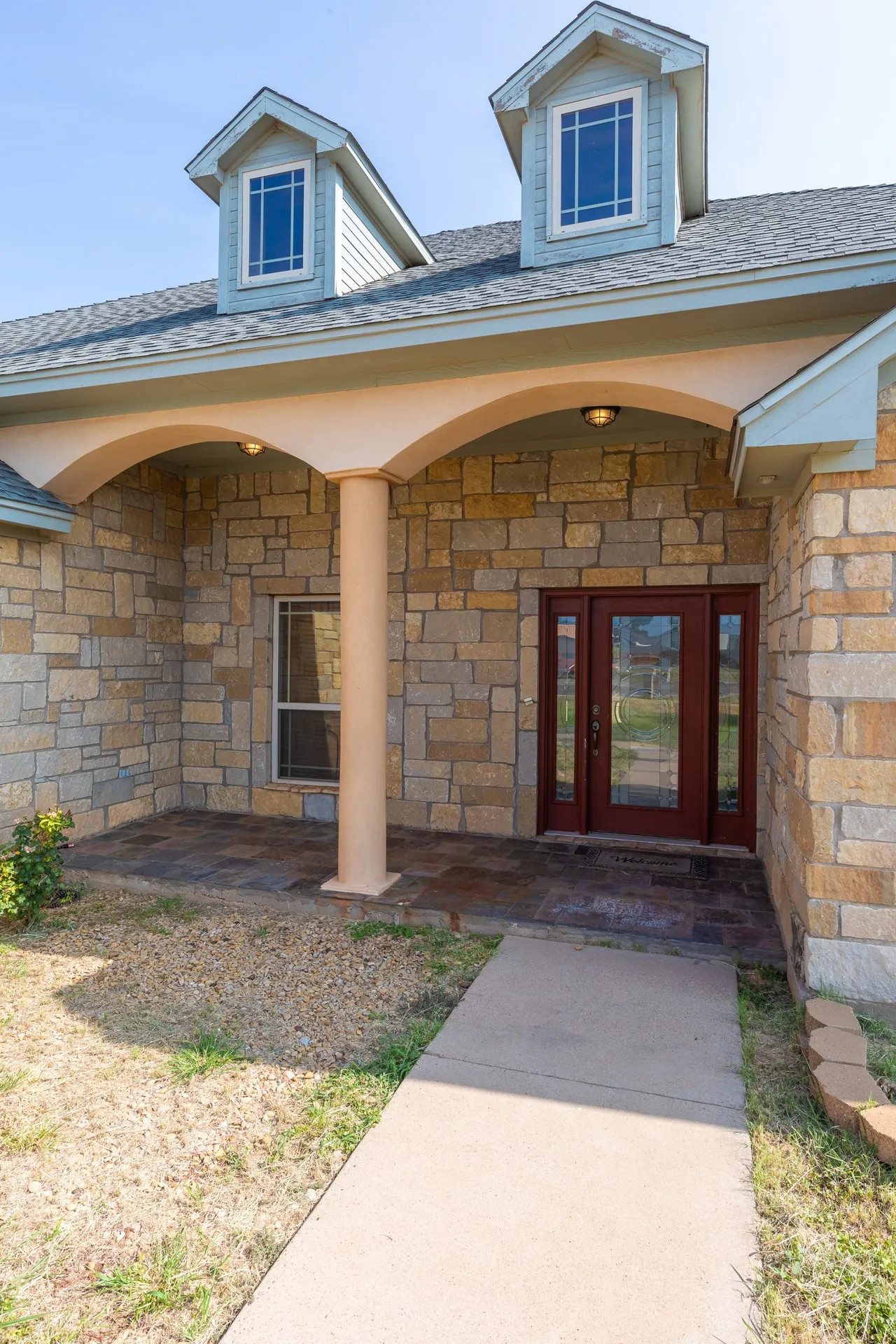 Welcoming covered entry features a barrel-vault ceiling with cream-colored soffit, complemented by warm-toned stone exterior walls and decorative columns