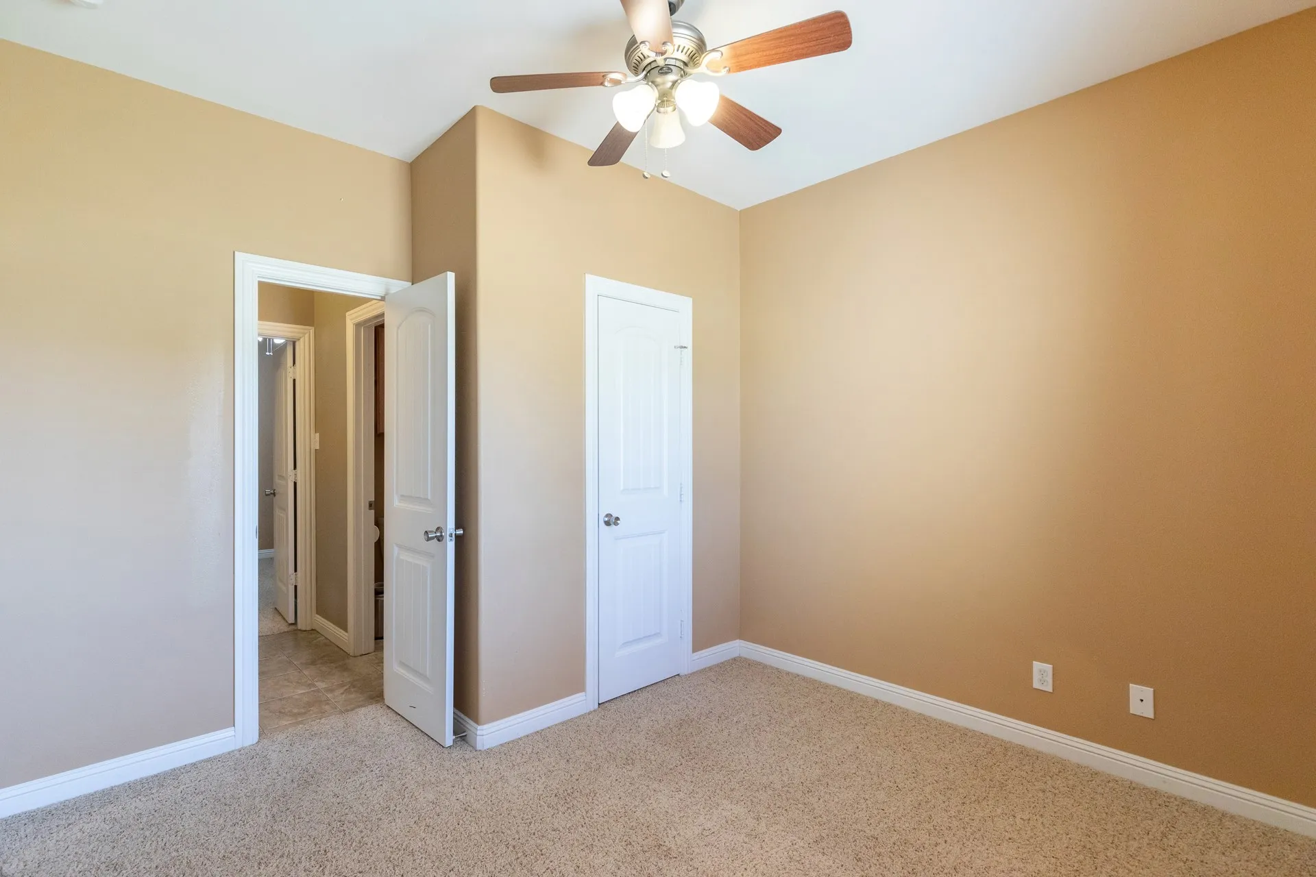 Spacious bedroom featuring neutral wall finishes, plush carpet flooring, ceiling fan with brushed nickel fixtures, and multiple white six-panel doors providing access to adjoining spaces