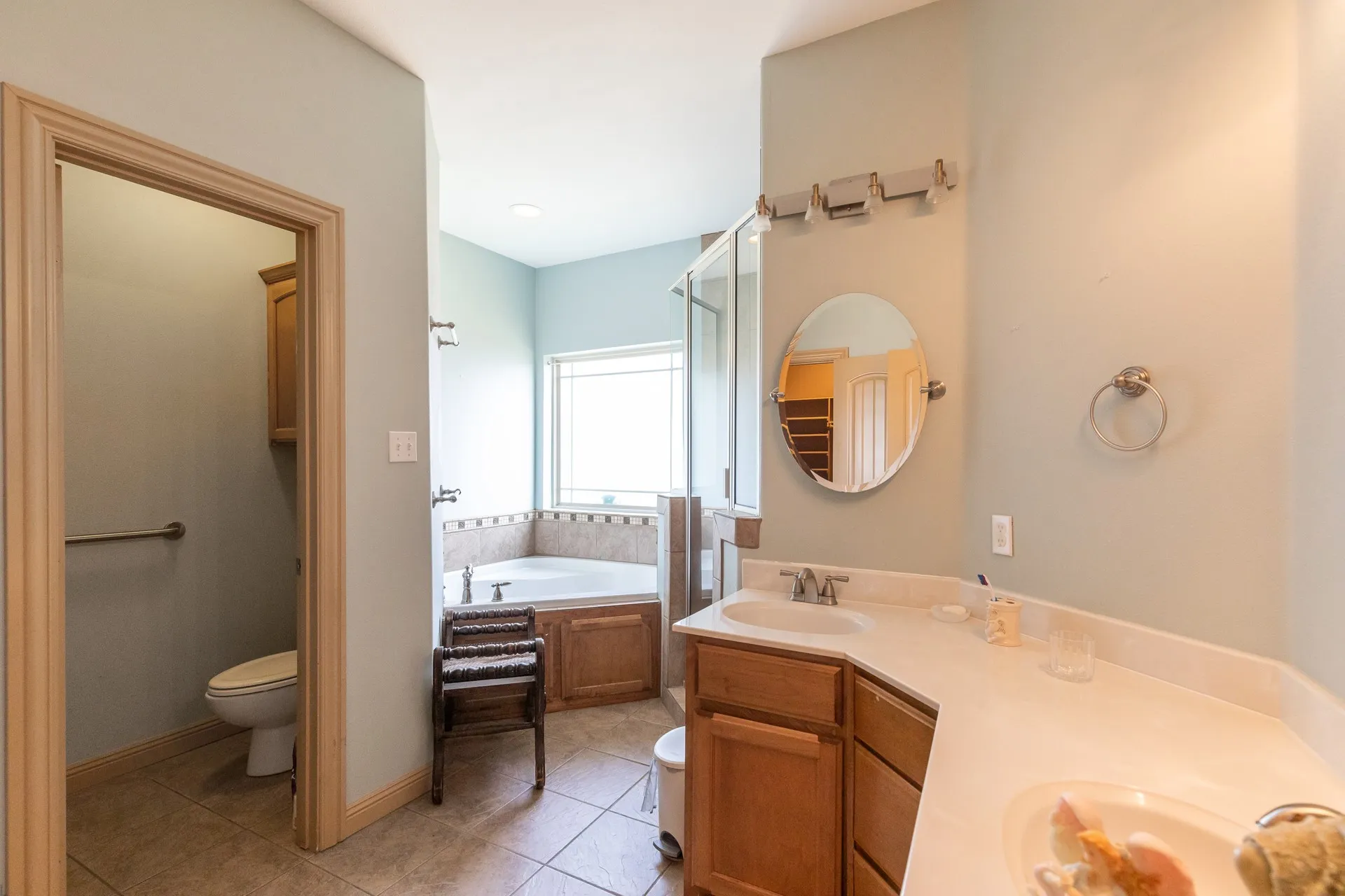 Bathroom featuring a corner soaking tub with tiled surround, a separate glass-enclosed shower, dual vanity with undermount sinks, and ceramic tile flooring
