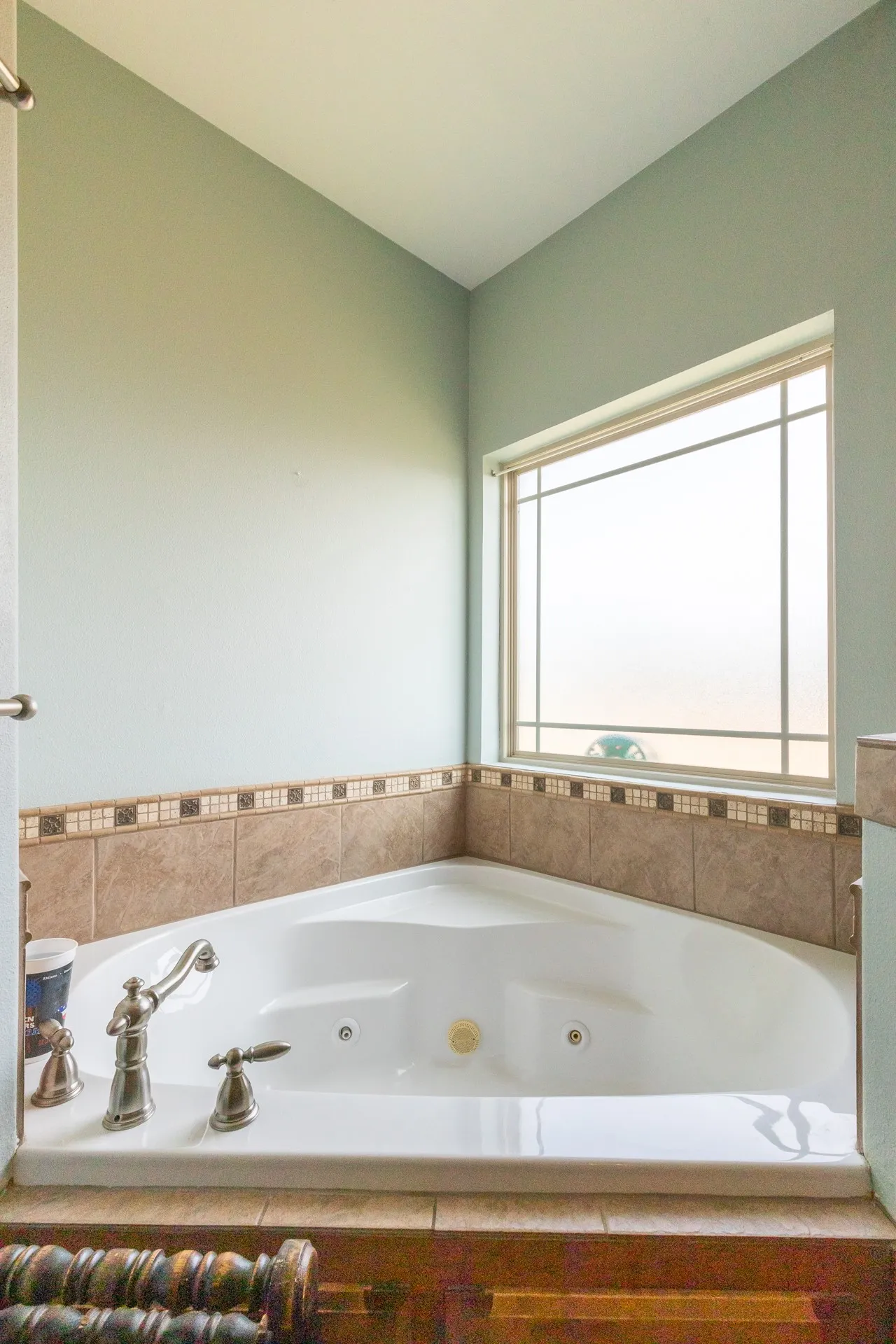 Corner jetted tub featuring a tile surround, decorative accent tiling, and a window with grid detailing