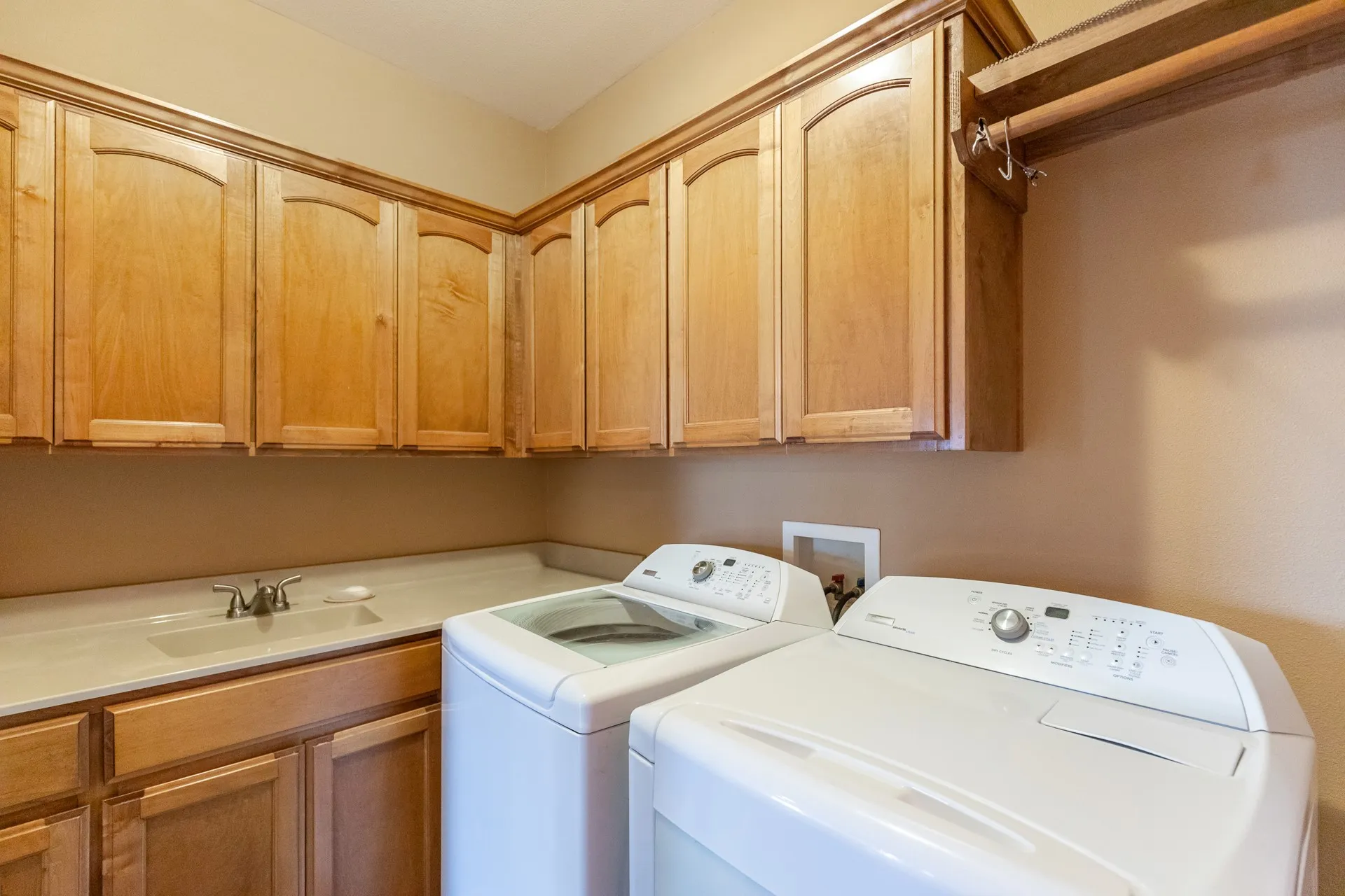 Laundry room featuring extensive wood cabinetry, an integrated sink with a countertop, and a built-in hanging rod
