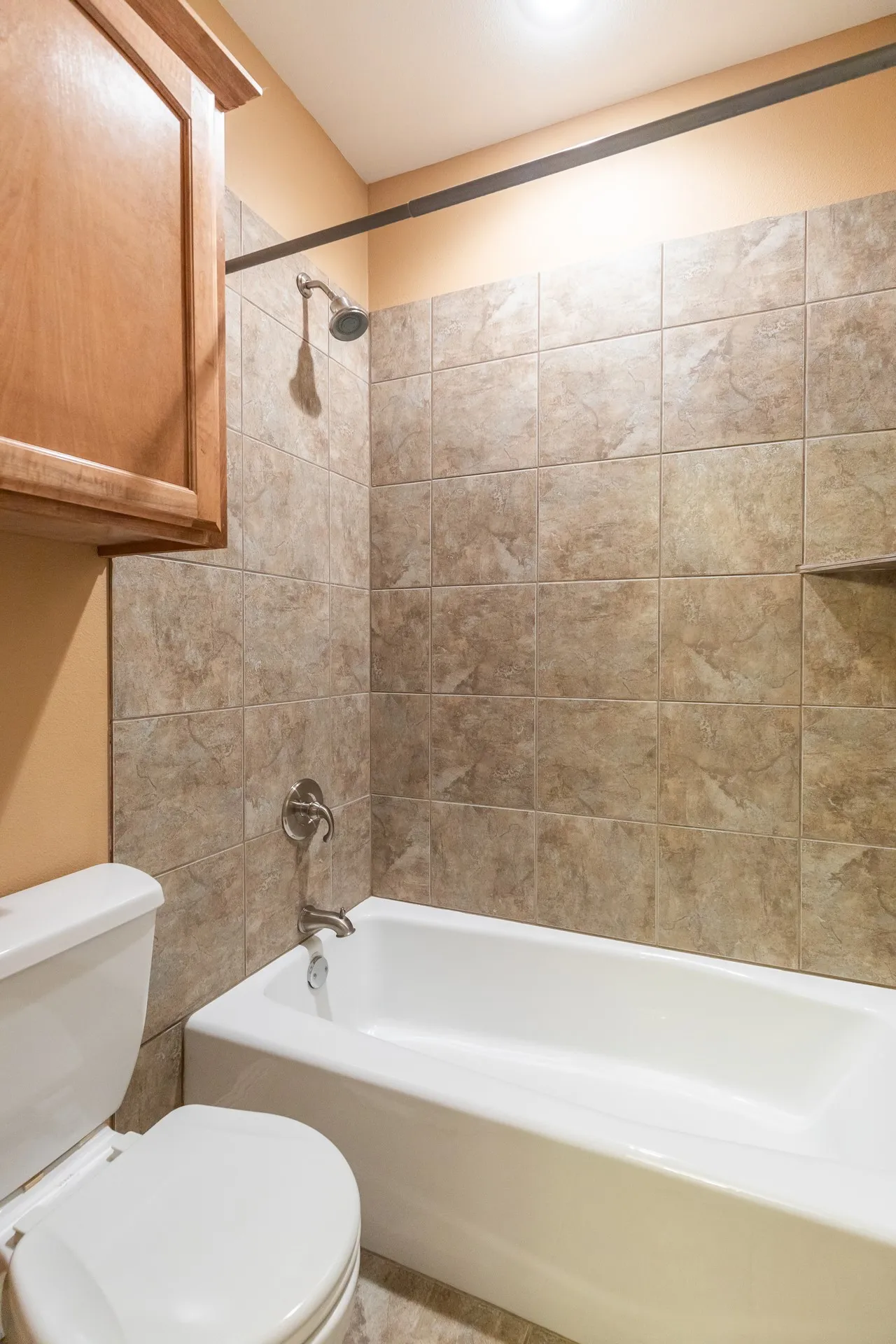 Bathroom featuring a white porcelain tub, shower with ceramic tile surround, recessed shelf, and brushed nickel fixtures