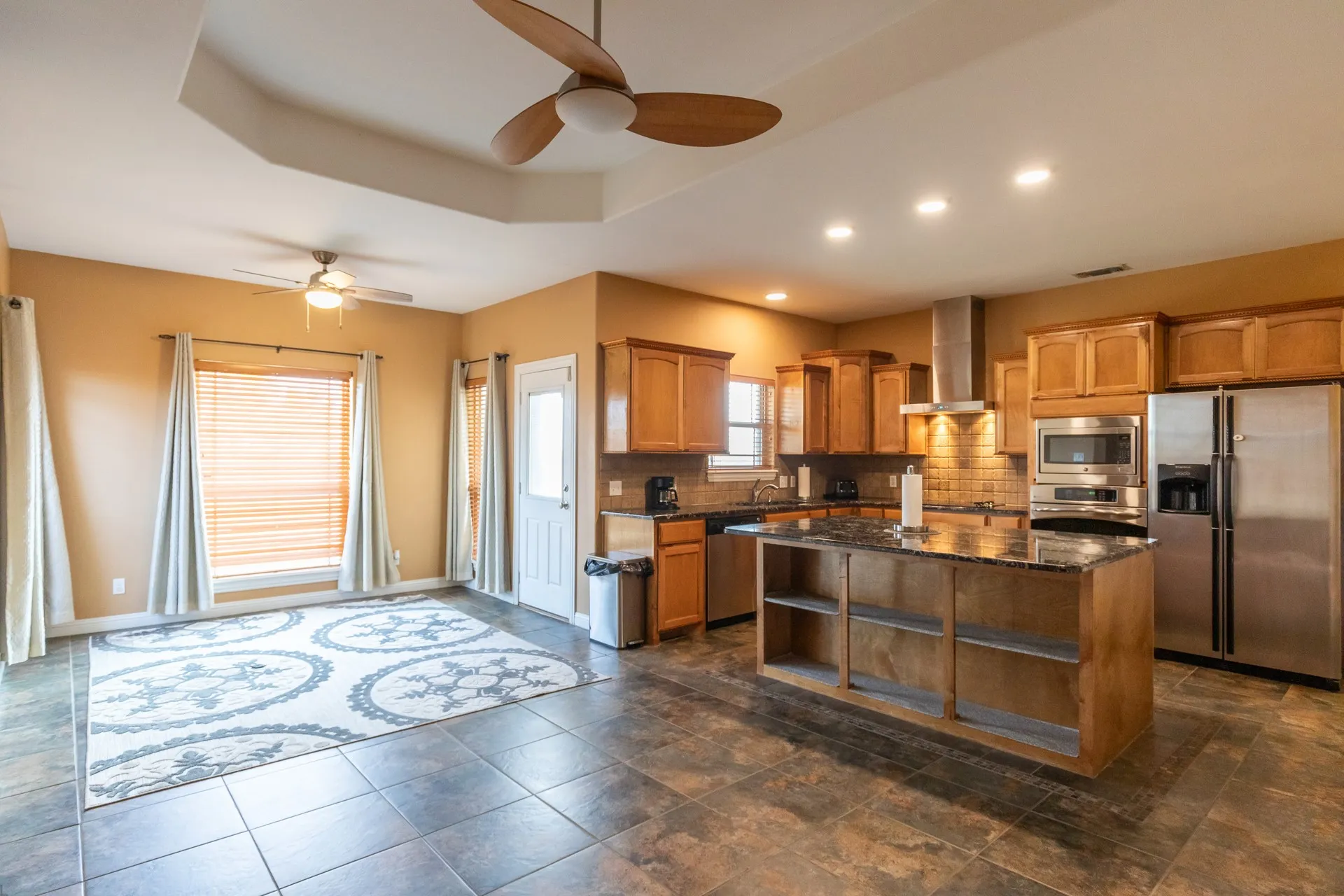 Open-concept living space featuring a spacious kitchen island with storage, wood-finish cabinetry, stainless steel appliances, recessed lighting, and a tray ceiling